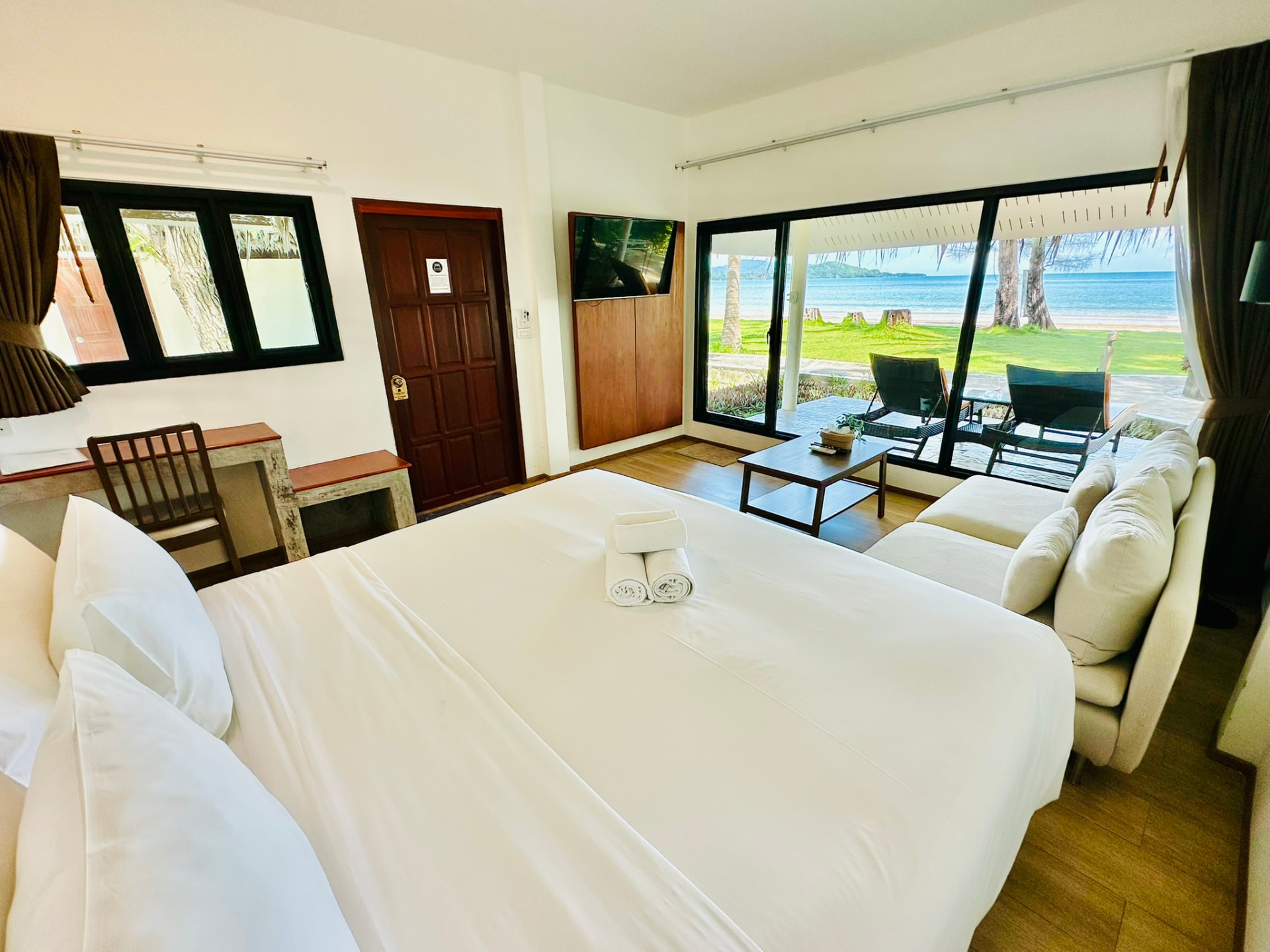 Wide view of a beachfront bungalow with king bed, writing desk, sofa and sea beyond