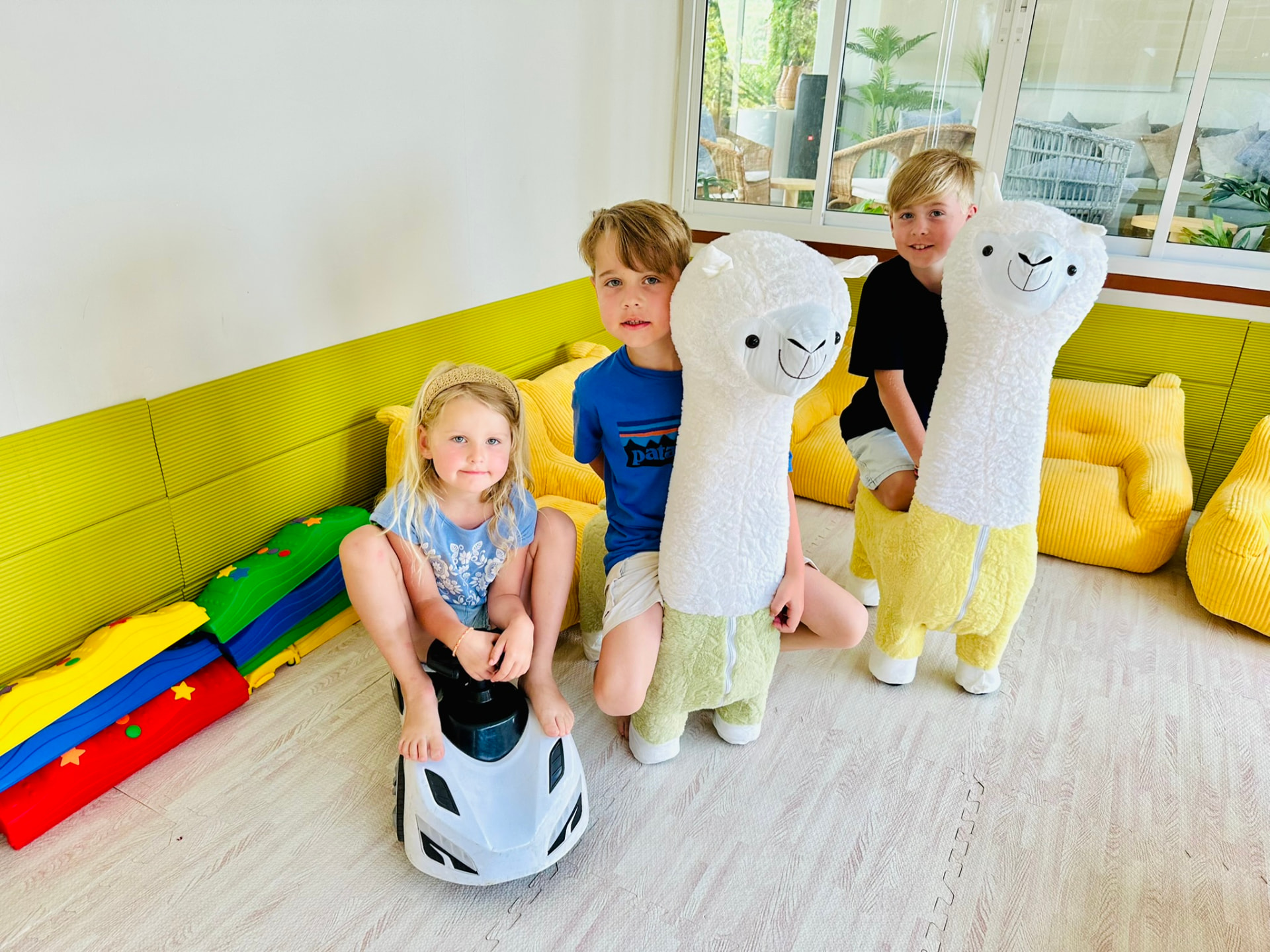 Three children posing with the soft alpaca ride-ons in the Kids Room