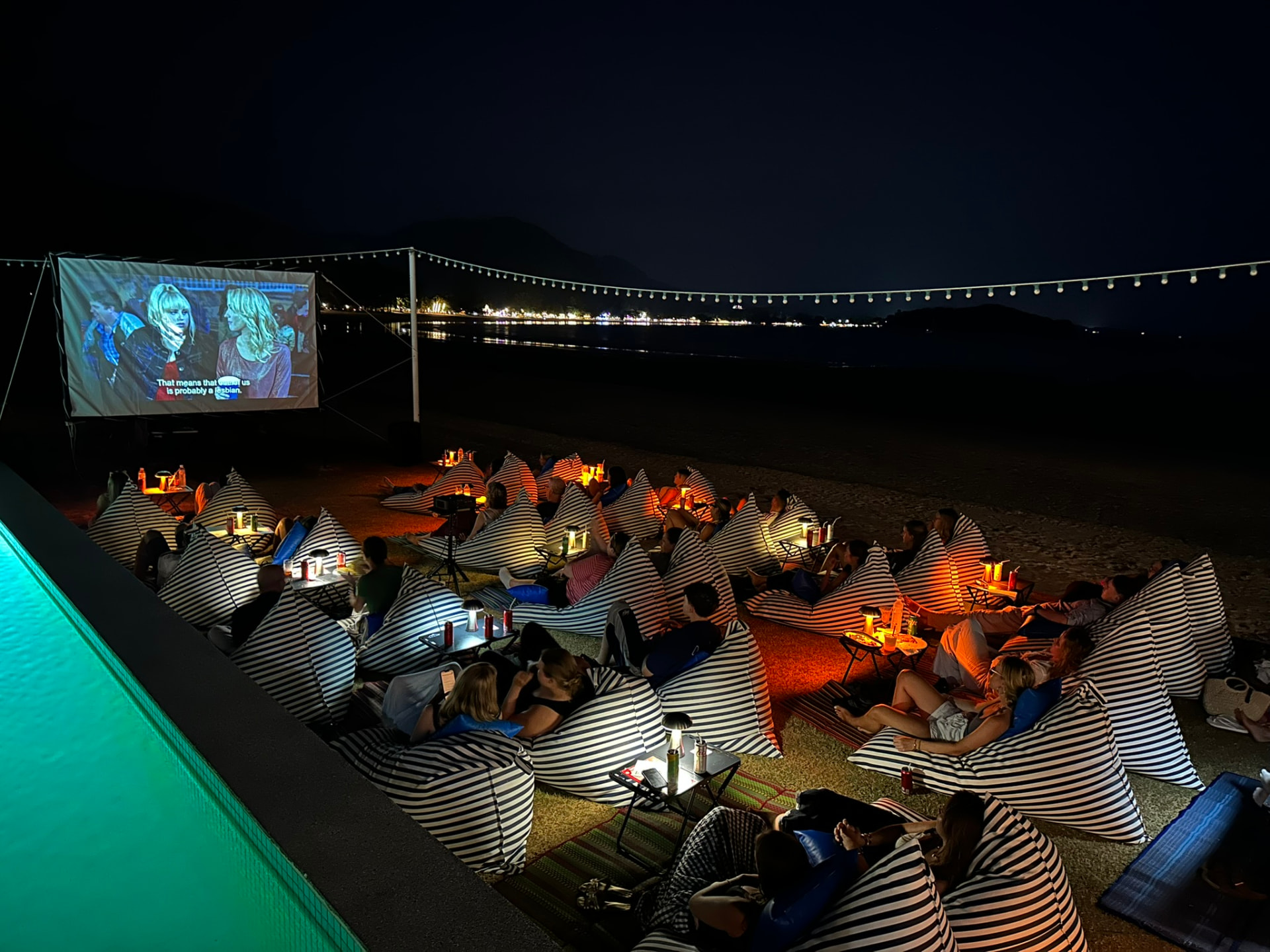 A film playing on a screen beside the pool with the bay lit up behind