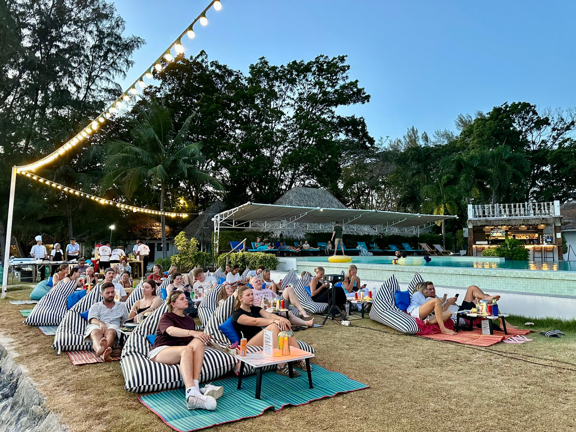 Guests on bean bags by the pool in the early evening waiting for the film