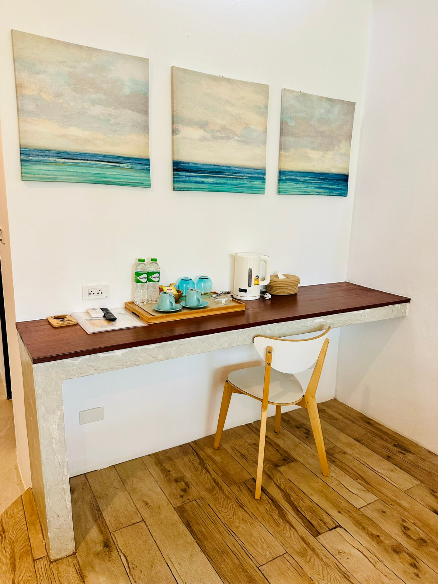 Long teak writing desk with kettle, tea tray and seascape canvases above