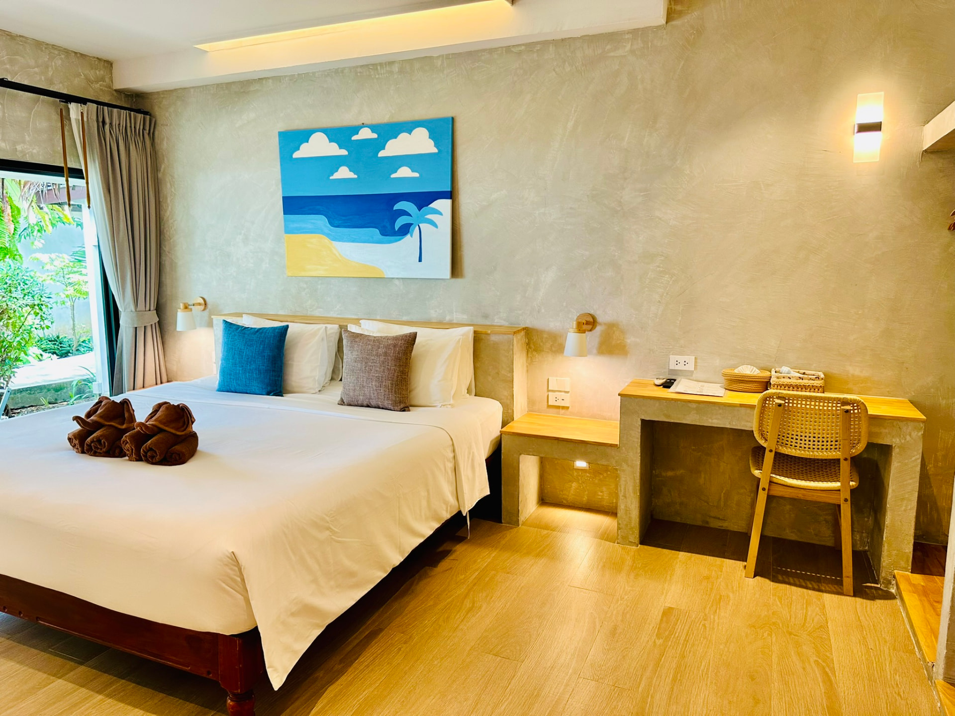 King bed with painted beach artwork above and a long wooden writing desk
