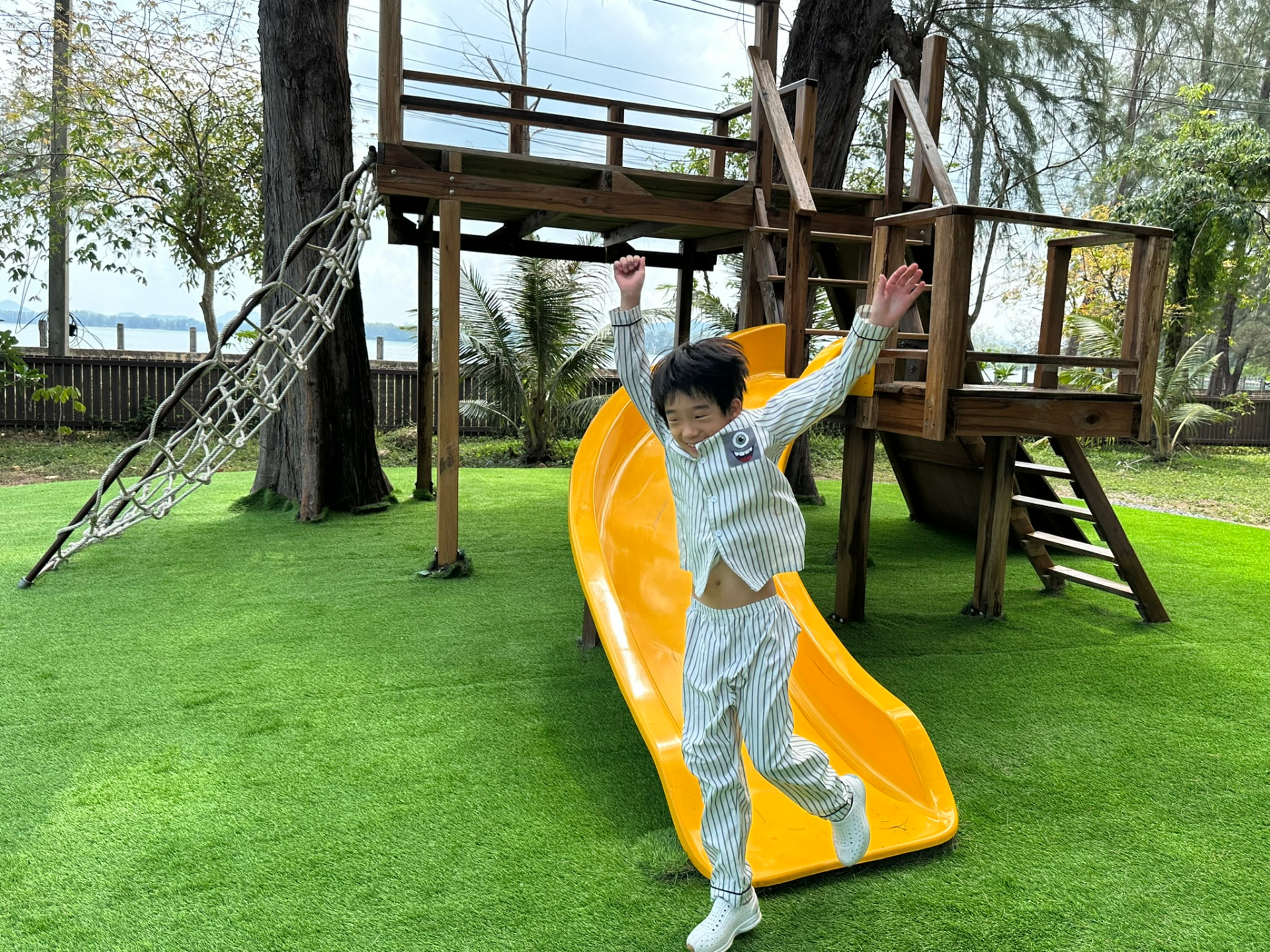 A boy landing at the bottom of the yellow slide with his arms in the air