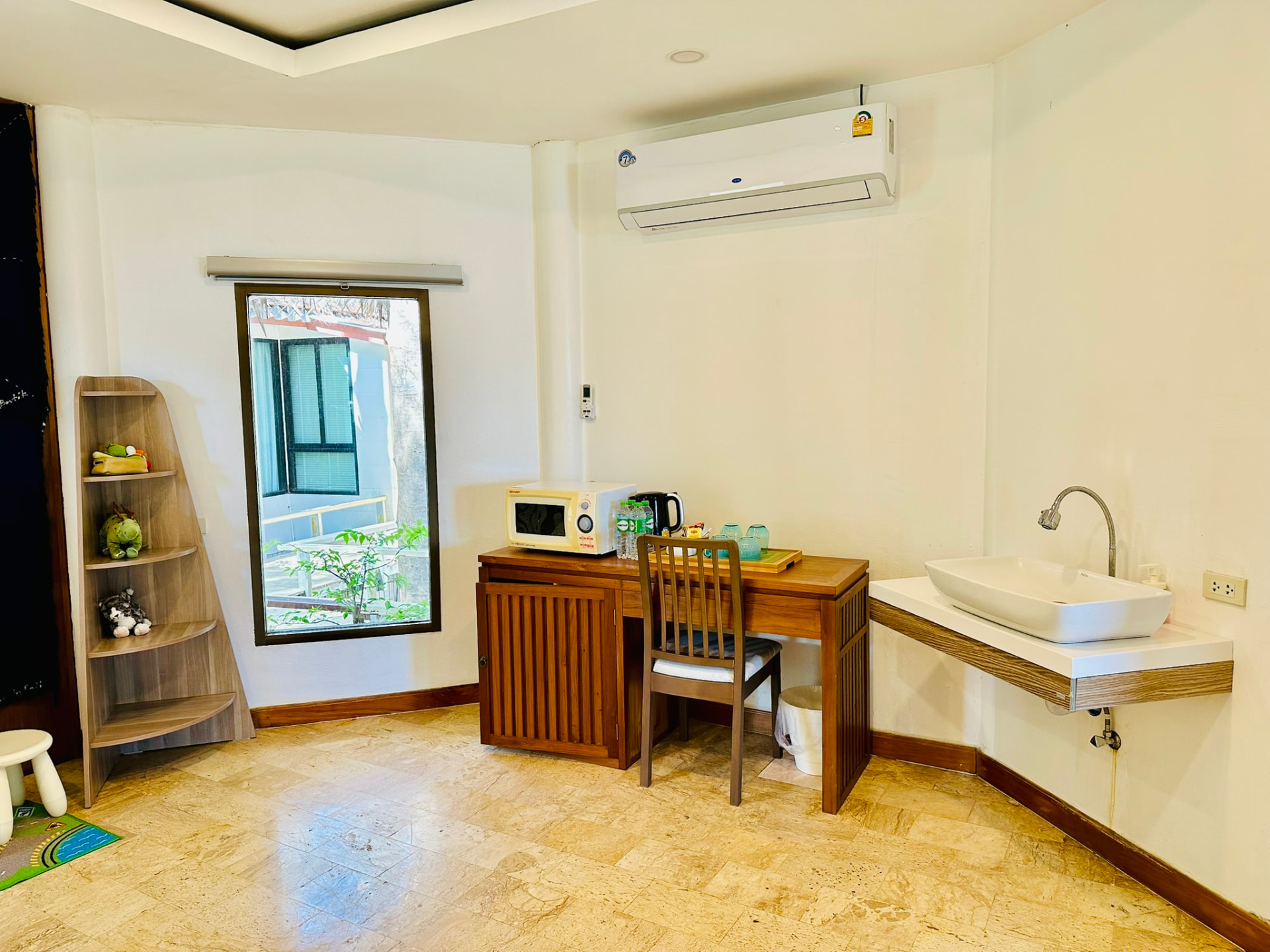 Teak desk with kettle, microwave and tea tray beside a basin and a garden window