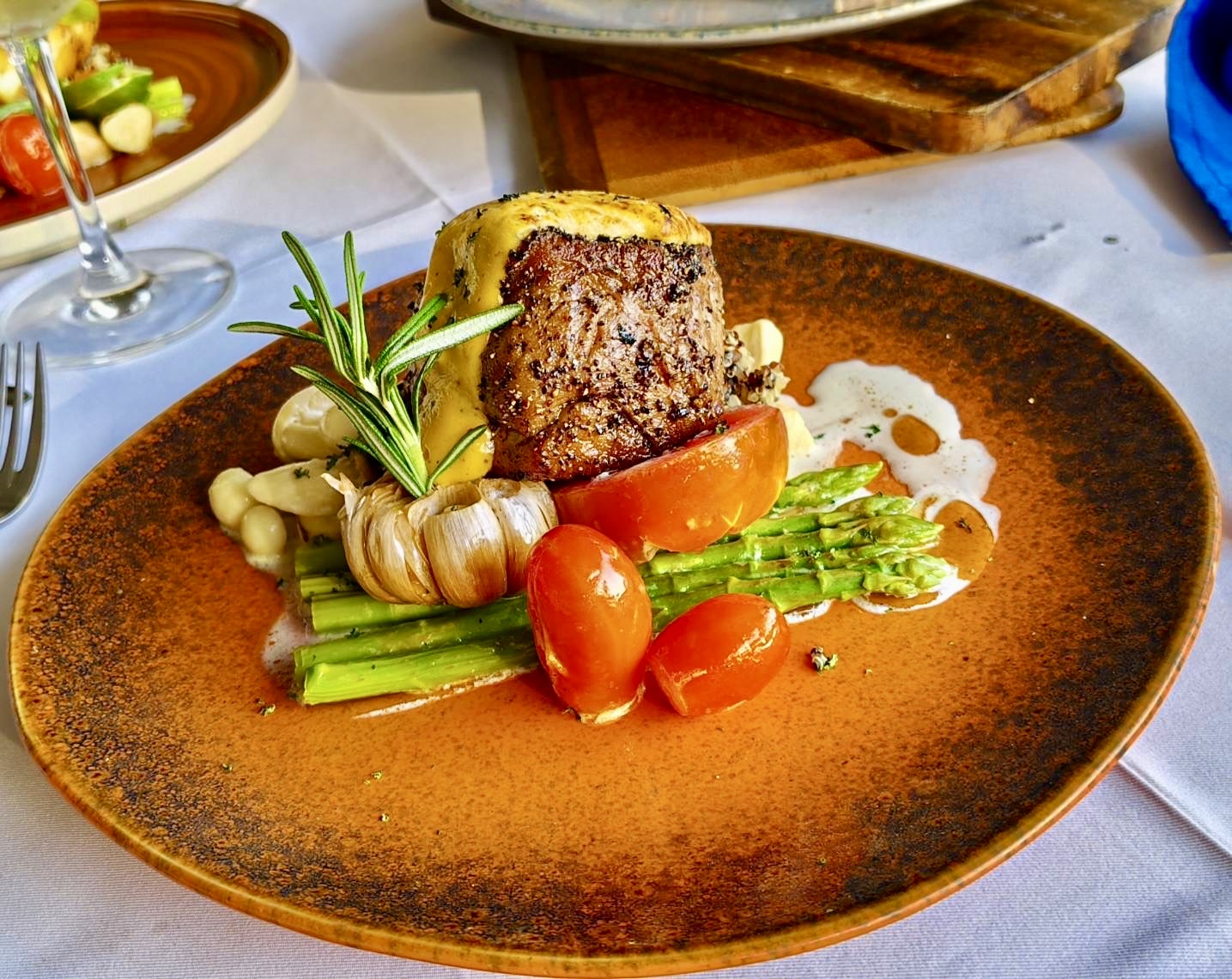 Steak with asparagus and tomatoes plated on a terracotta dish
