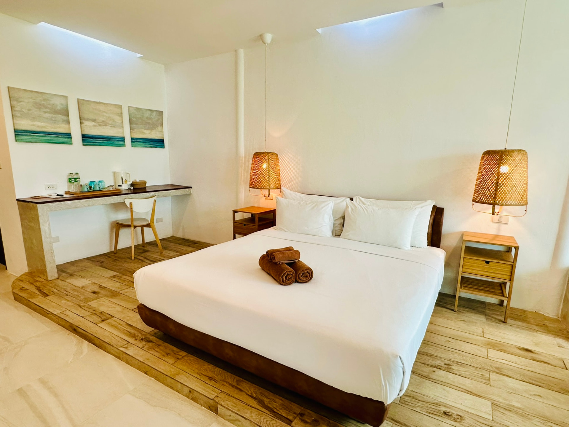 King bed beside a writing desk with tea tray and three seascape canvases