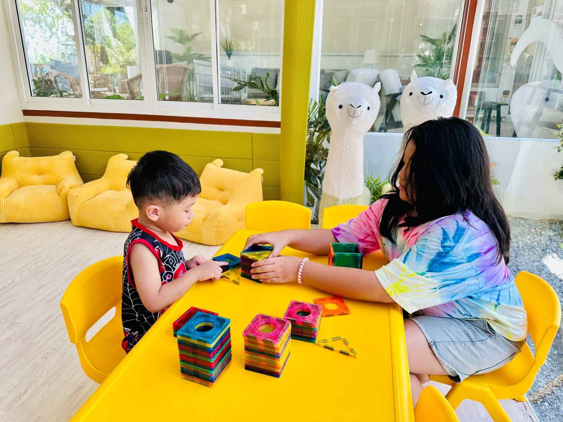 Two children stacking magnetic tiles at the yellow table in the Kids Room