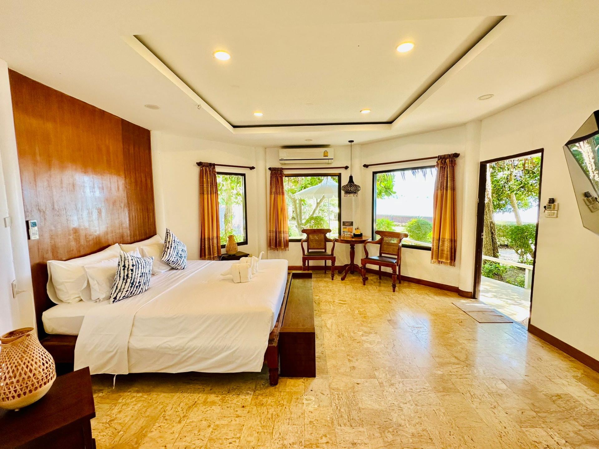 Wide main bedroom with a teak headboard, stone floor and windows onto the garden and the bay