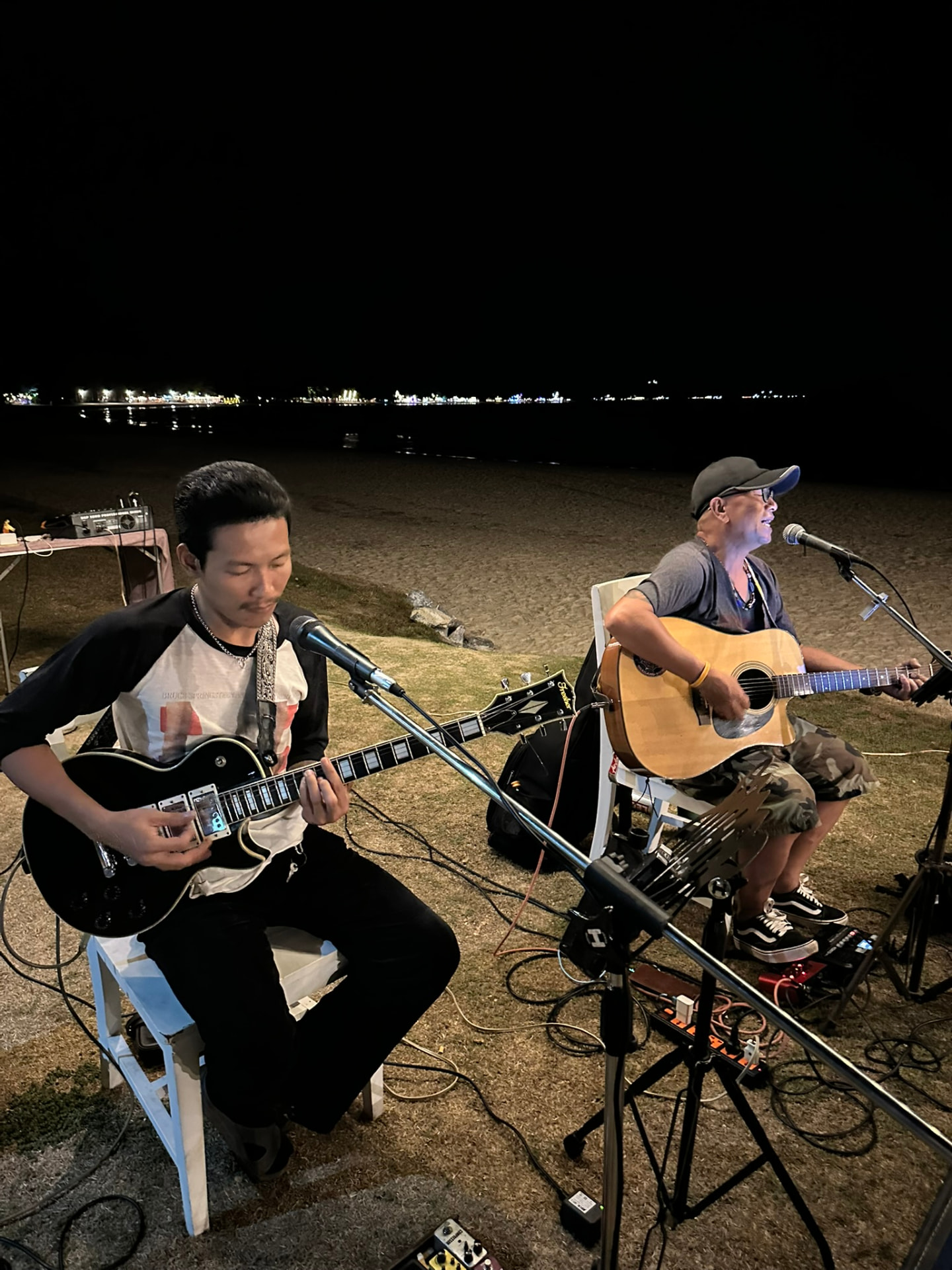 Two local musicians playing electric and acoustic guitar on the grass beside the beach