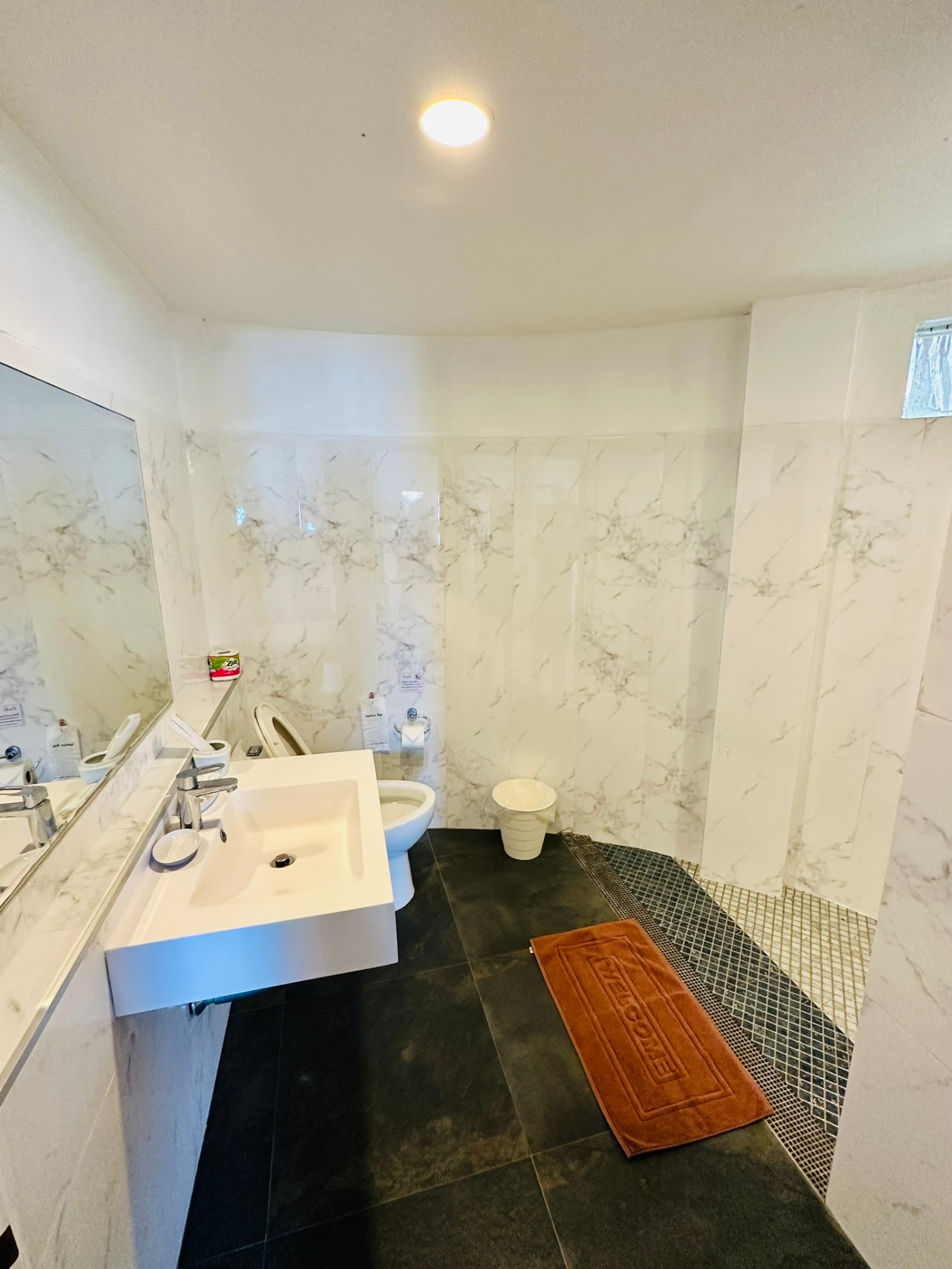 Marble bathroom with a floating basin, wide mirror and dark stone floor