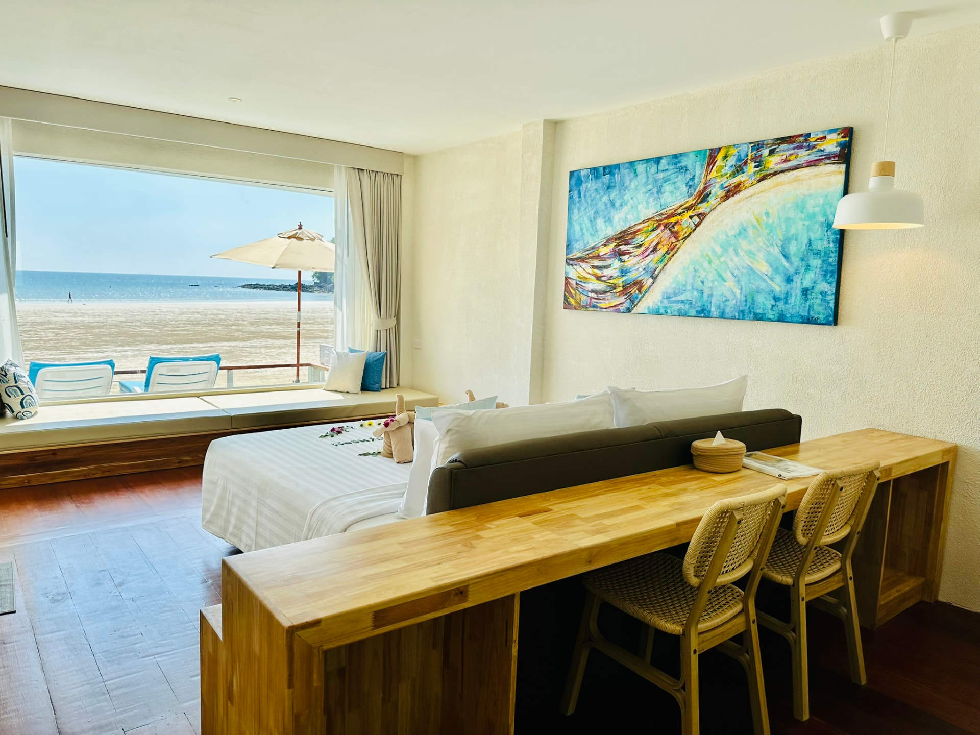 Long timber writing desk with rattan chairs, sofa and the beach through the window