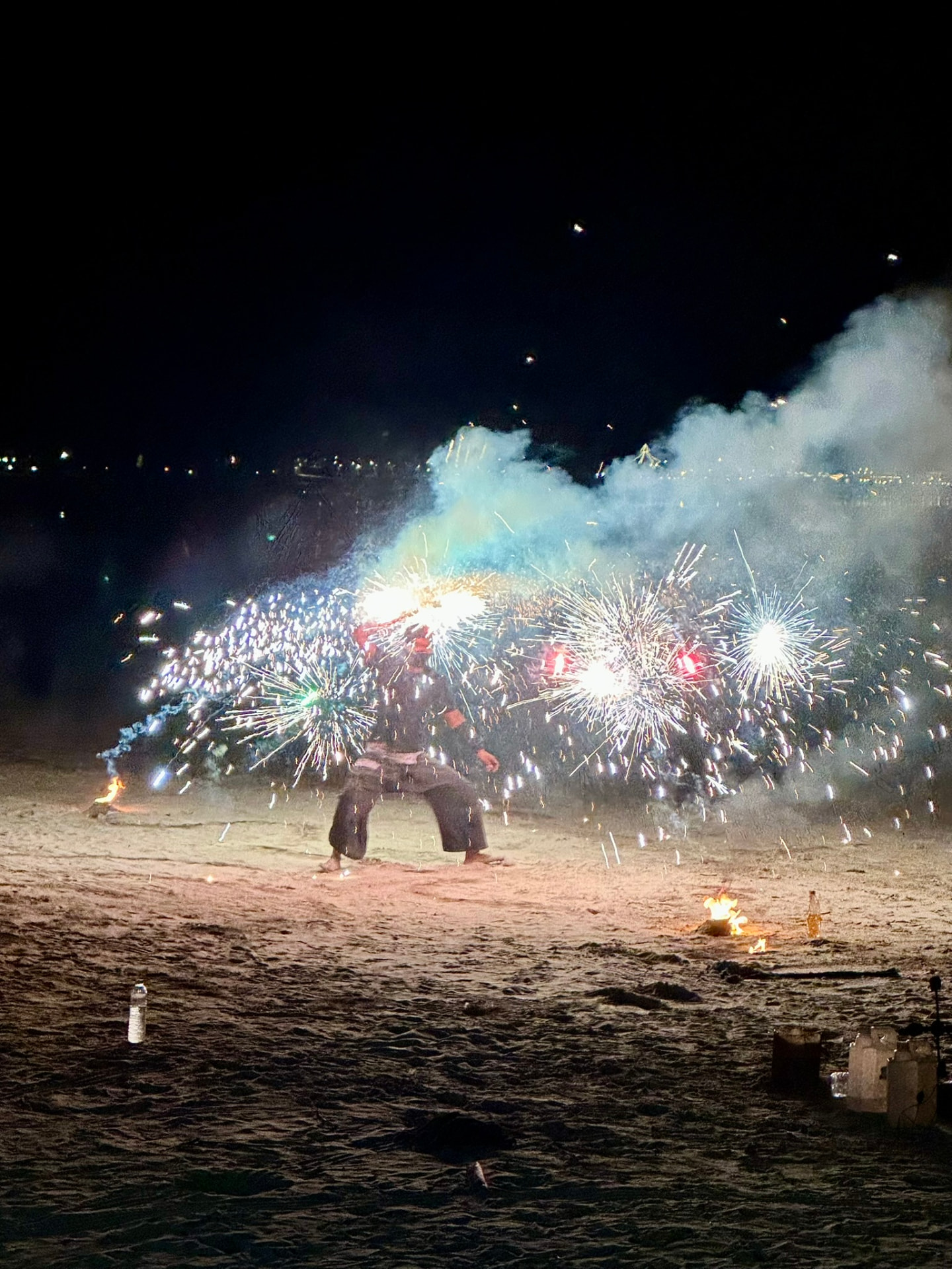 A fire performer surrounded by a burst of white sparks on the dark beach