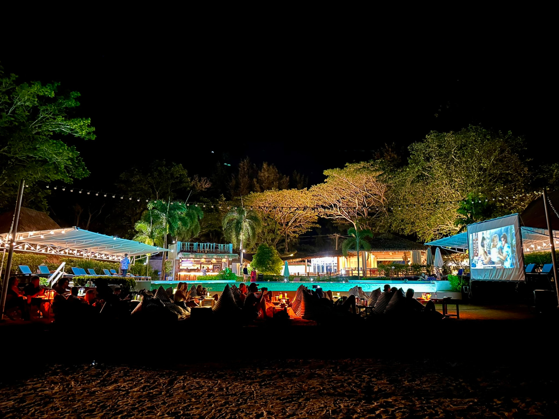 The lit pool, bar and film screen seen from the beach at night