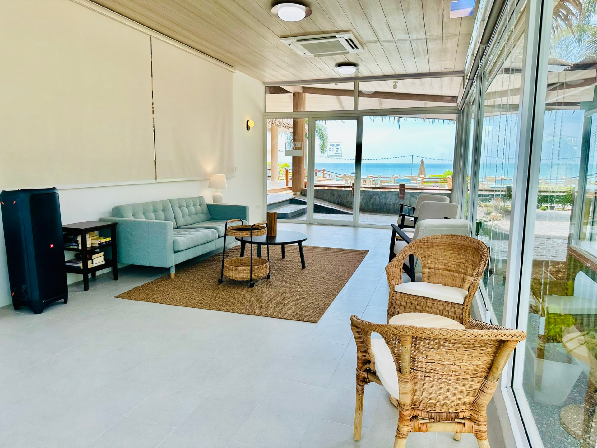 Sofa and rattan chairs in the Living Lounge facing open doors to the beach