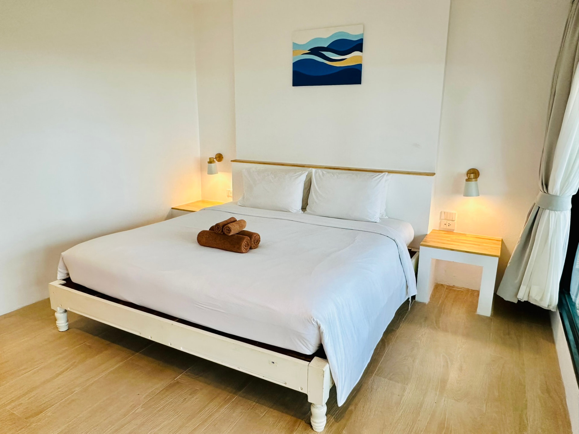 King bed with folded towels beneath a hand-painted wave artwork