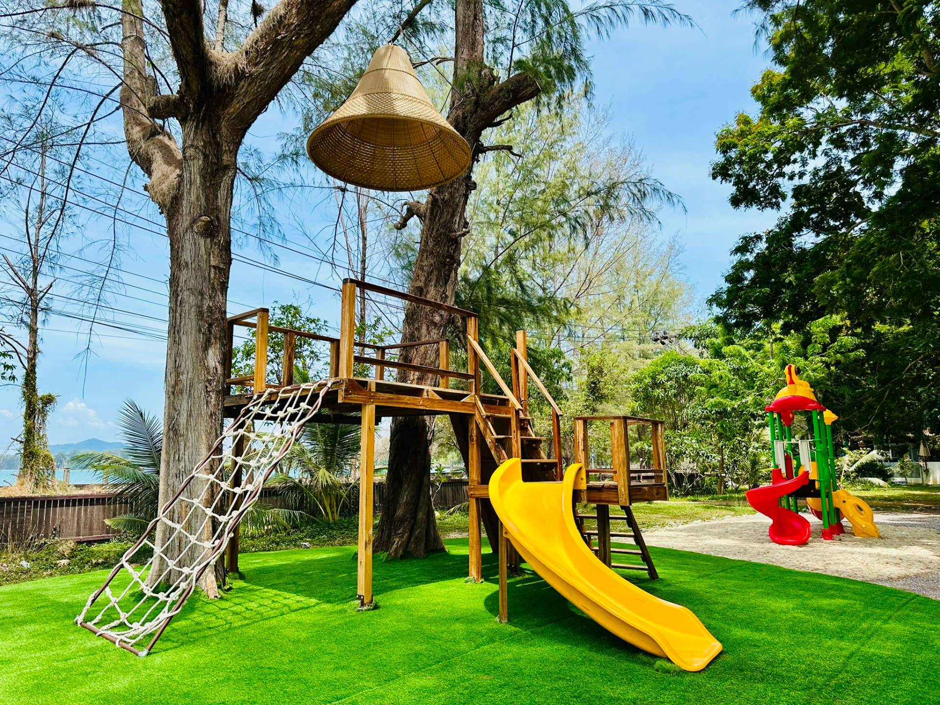 Wooden treehouse with a rope net and yellow slide under the casuarina trees