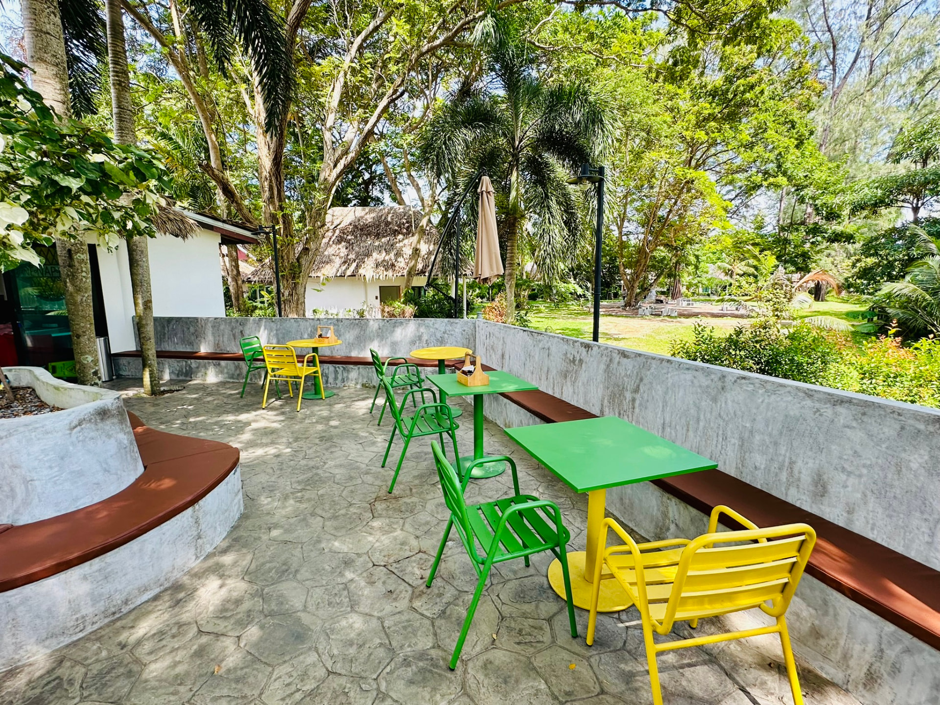 Shaded terrace tables at PineNapple Cafe with bungalows and gardens behind