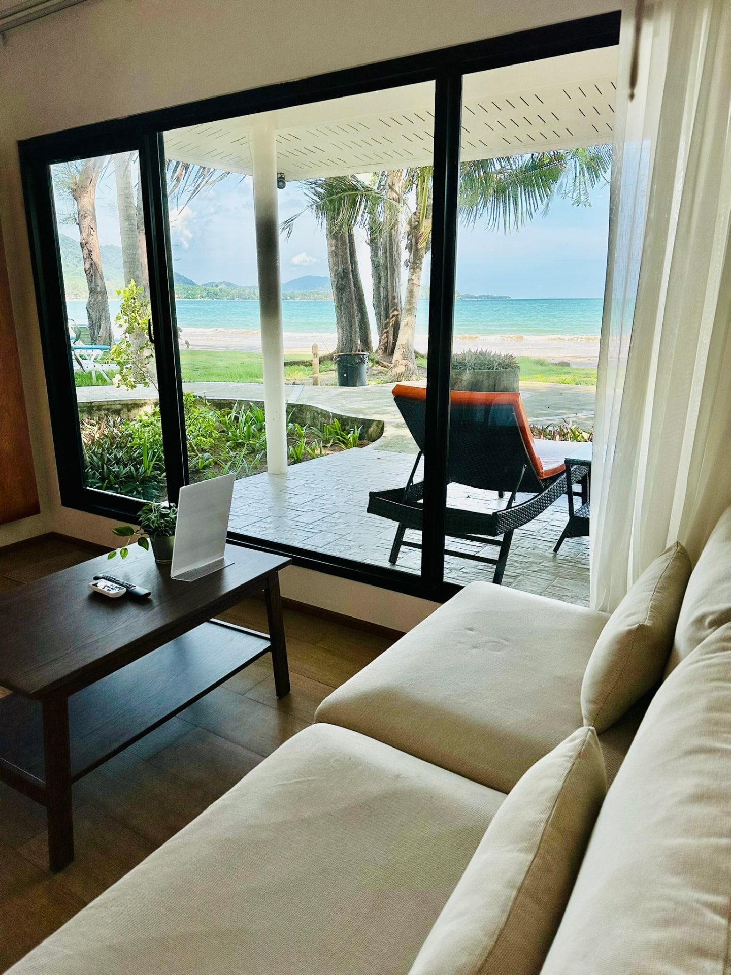 Sofa and coffee table looking out to the veranda sunbeds, palms and turquoise sea