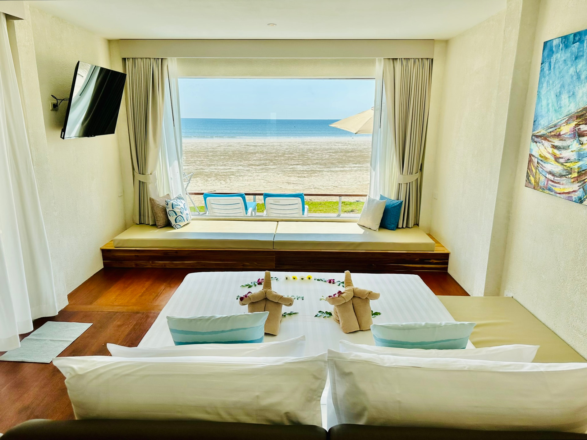King bed facing a wide picture window with a day bed, sunbeds and the beach beyond