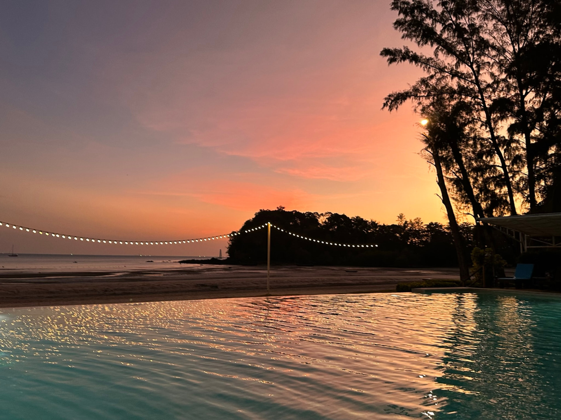 String lights and a pink sunset reflected in the pool
