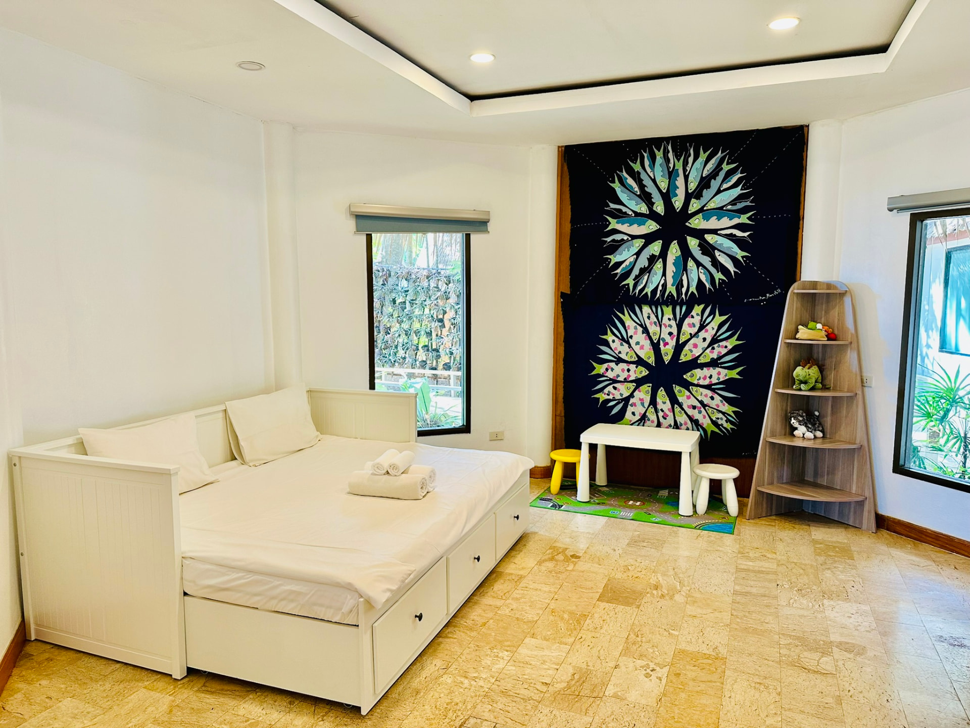 Second bedroom with a day bed, small table and stools, toy shelf and a batik wall hanging