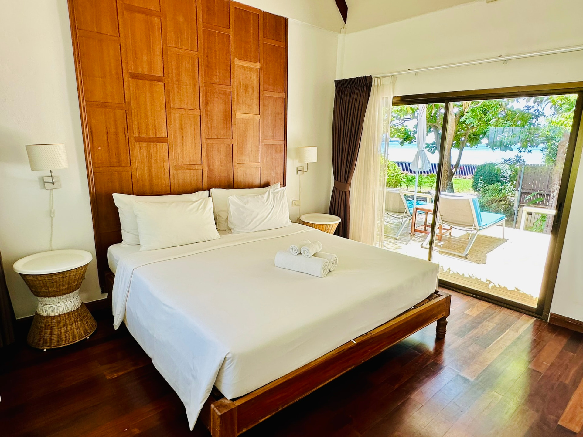 King bed with a carved teak headboard and sliding doors opening onto a sunbed terrace with the bay beyond