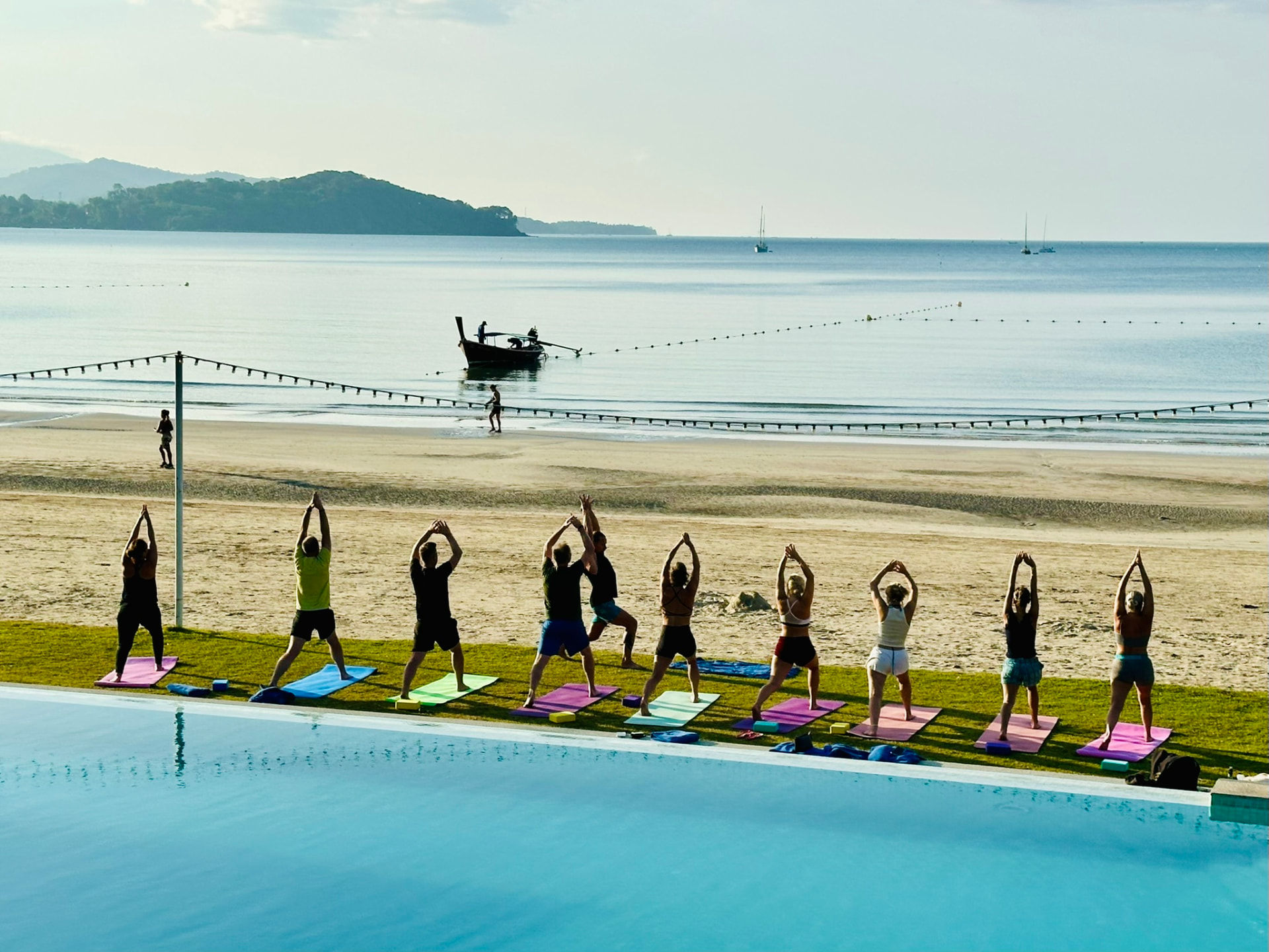 A yoga class in warrior pose beside the pool overlooking the bay