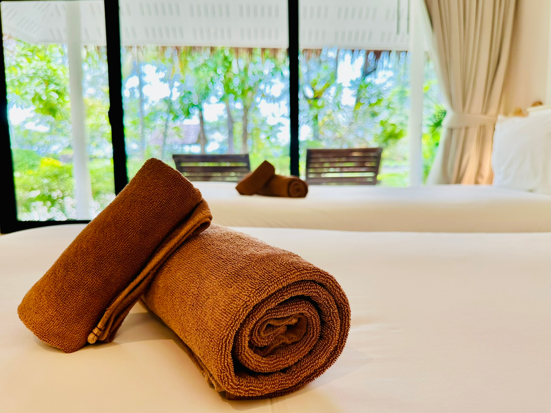Rolled towels on crisp white linen with the green garden beyond the window