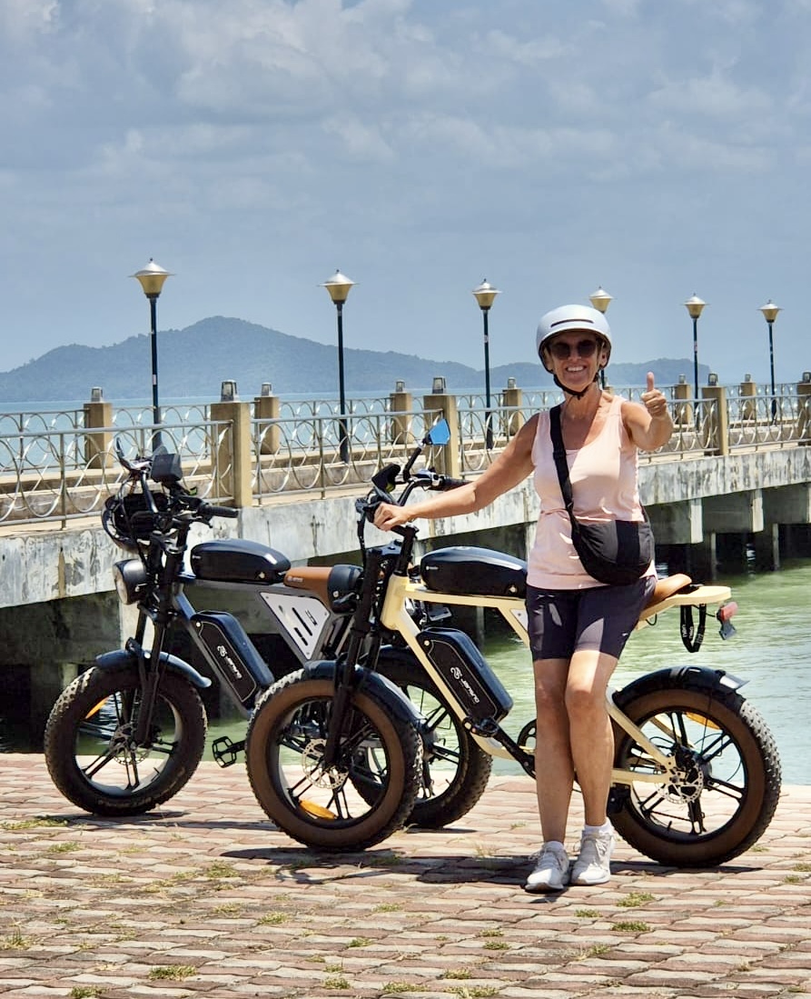 A guest giving a thumbs up beside her e-bike on the pier at Koh Lanta