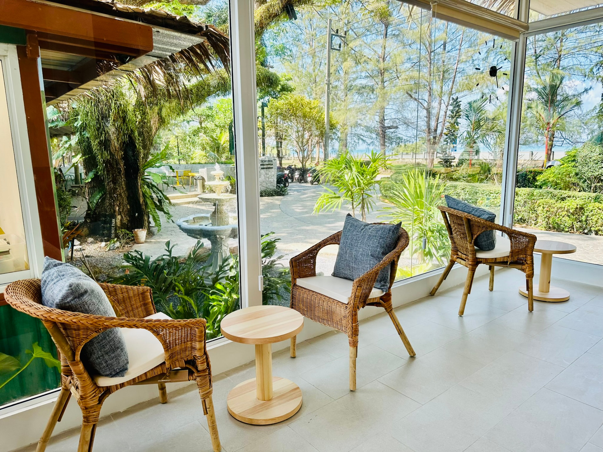 Rattan chairs and pine side tables along the glass wall facing the garden fountain