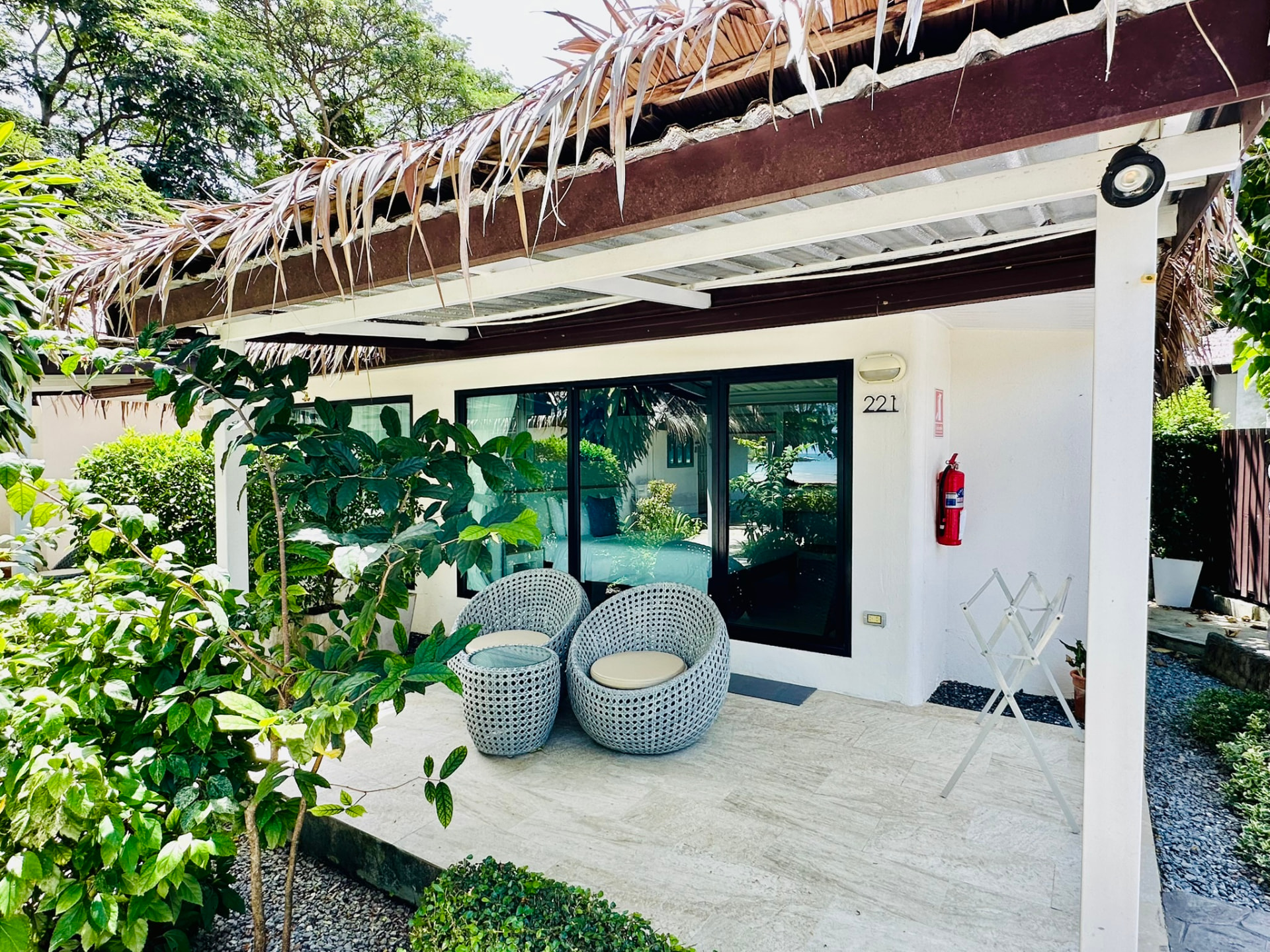 Thatched bungalow terrace with woven chairs surrounded by garden planting