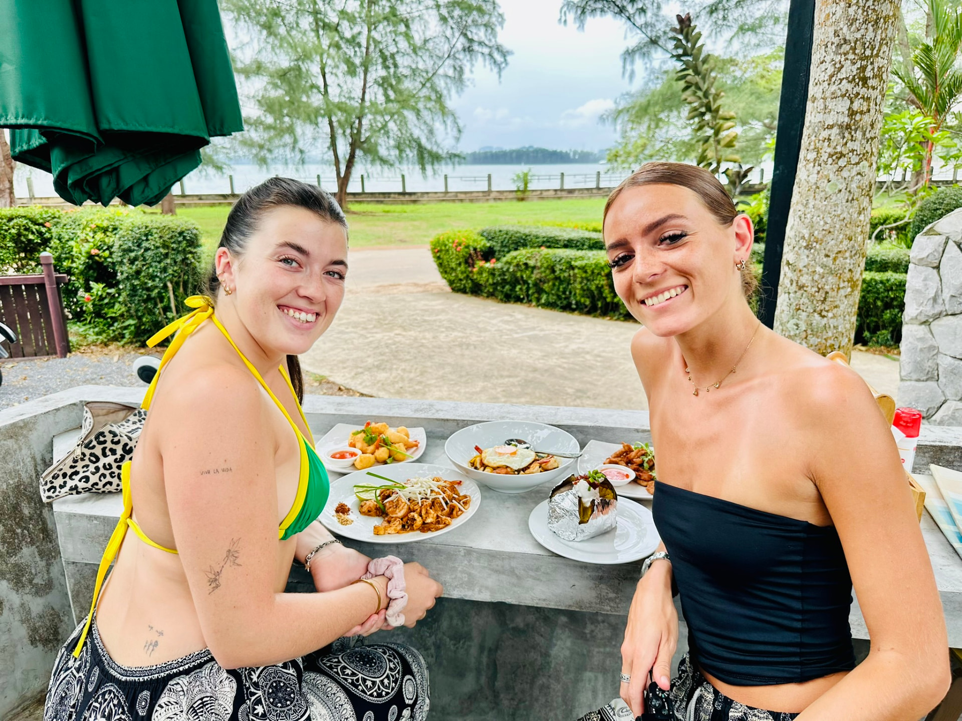 Two guests smiling over a spread of Thai dishes at the PineNapple Cafe bar counter