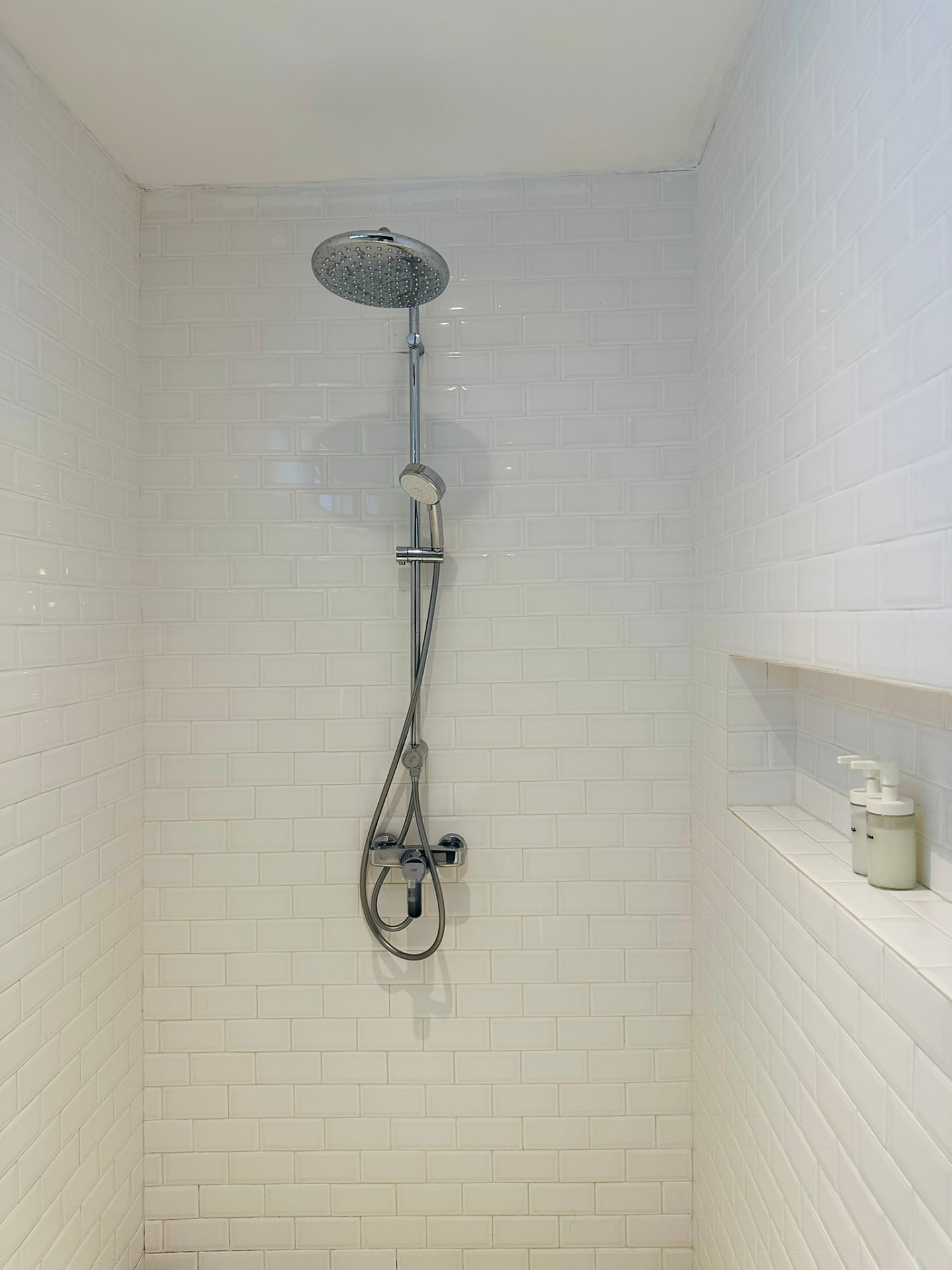 Walk-in rain shower with white metro tiles and a recessed shelf