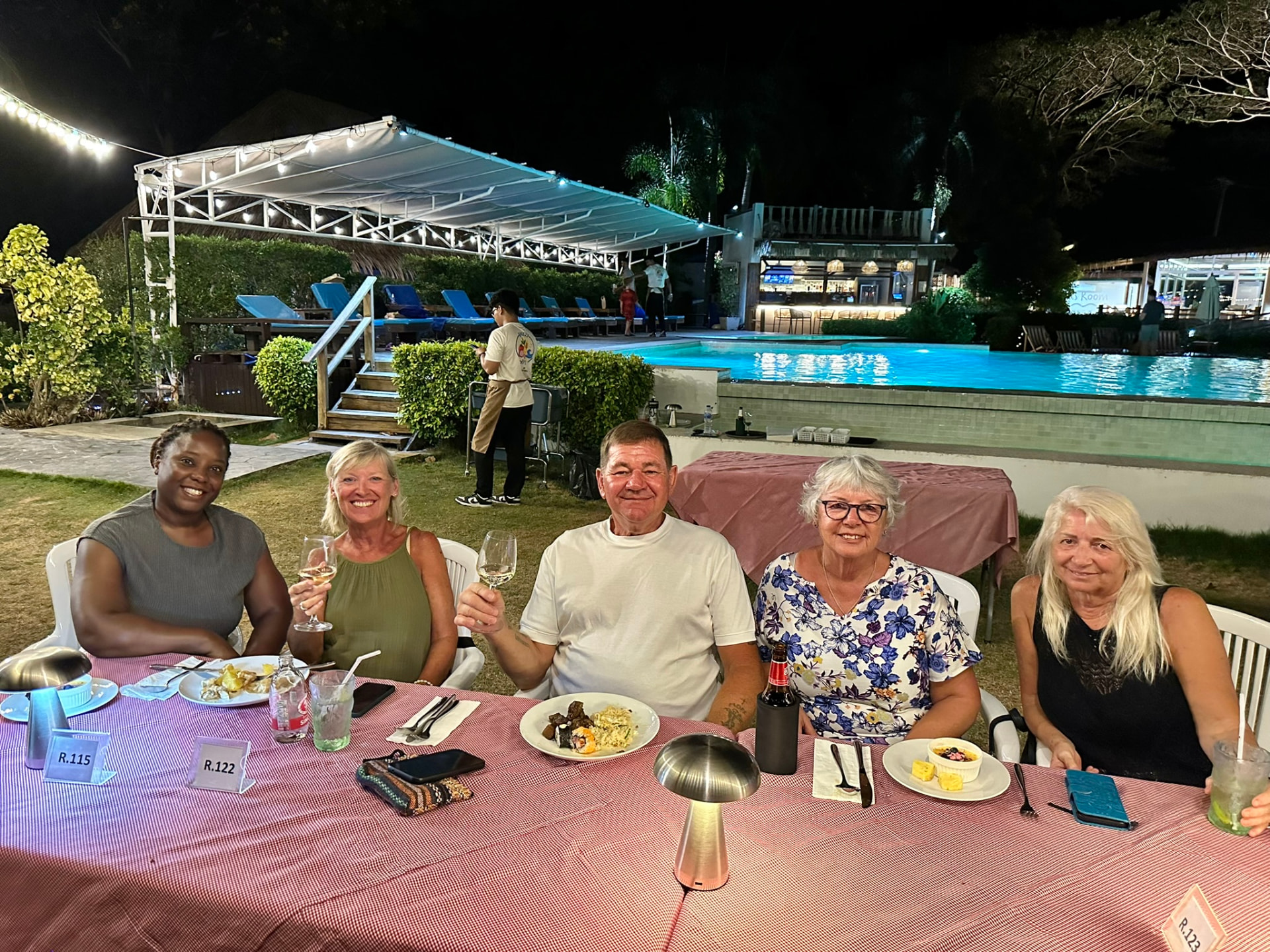 Five guests raising their glasses at a dinner table beside the floodlit pool