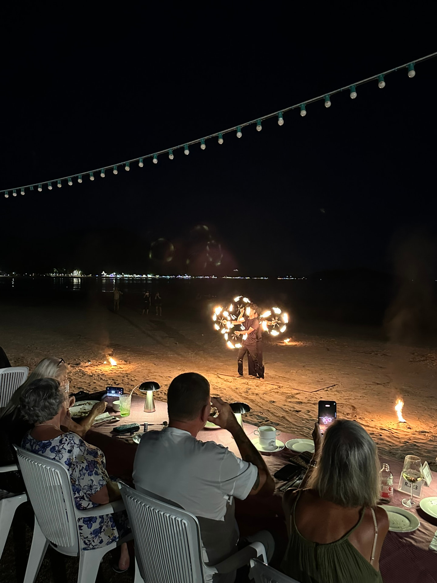 Guests filming a fire dancer spinning flaming hoops on the beach at night
