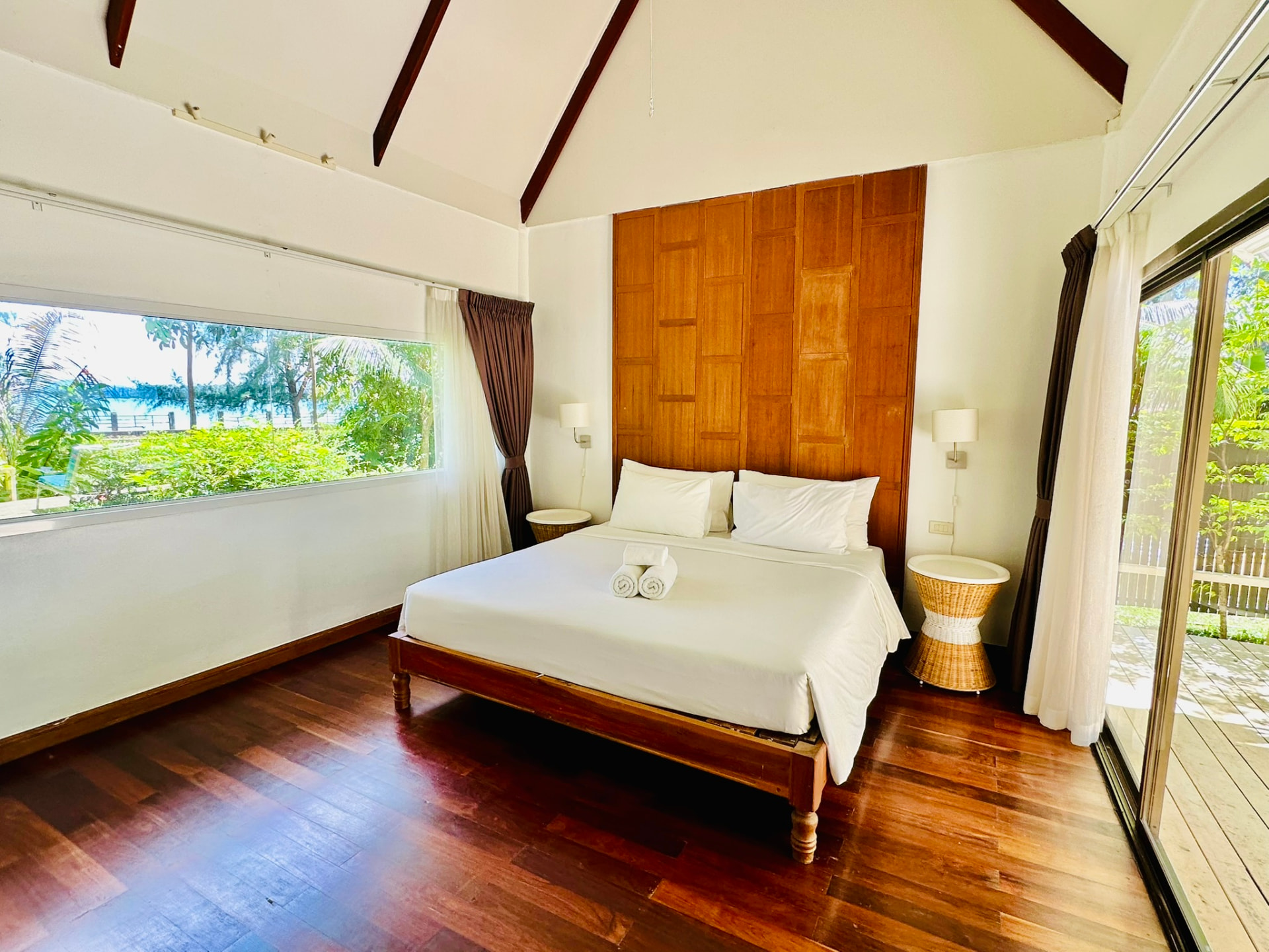 Bedroom with vaulted ceiling, dark timber beams and a picture window onto the garden
