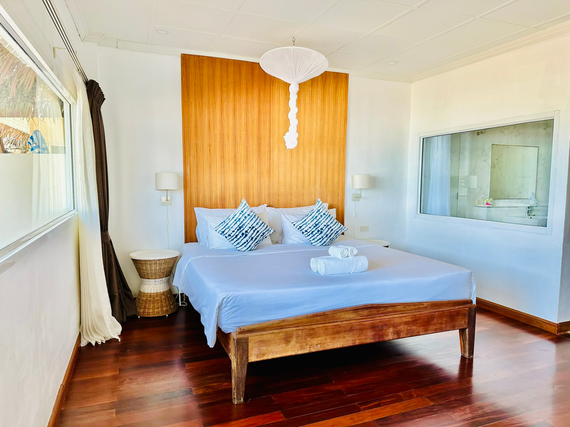 King bed with a teak panel headboard, paper lantern and rattan side table