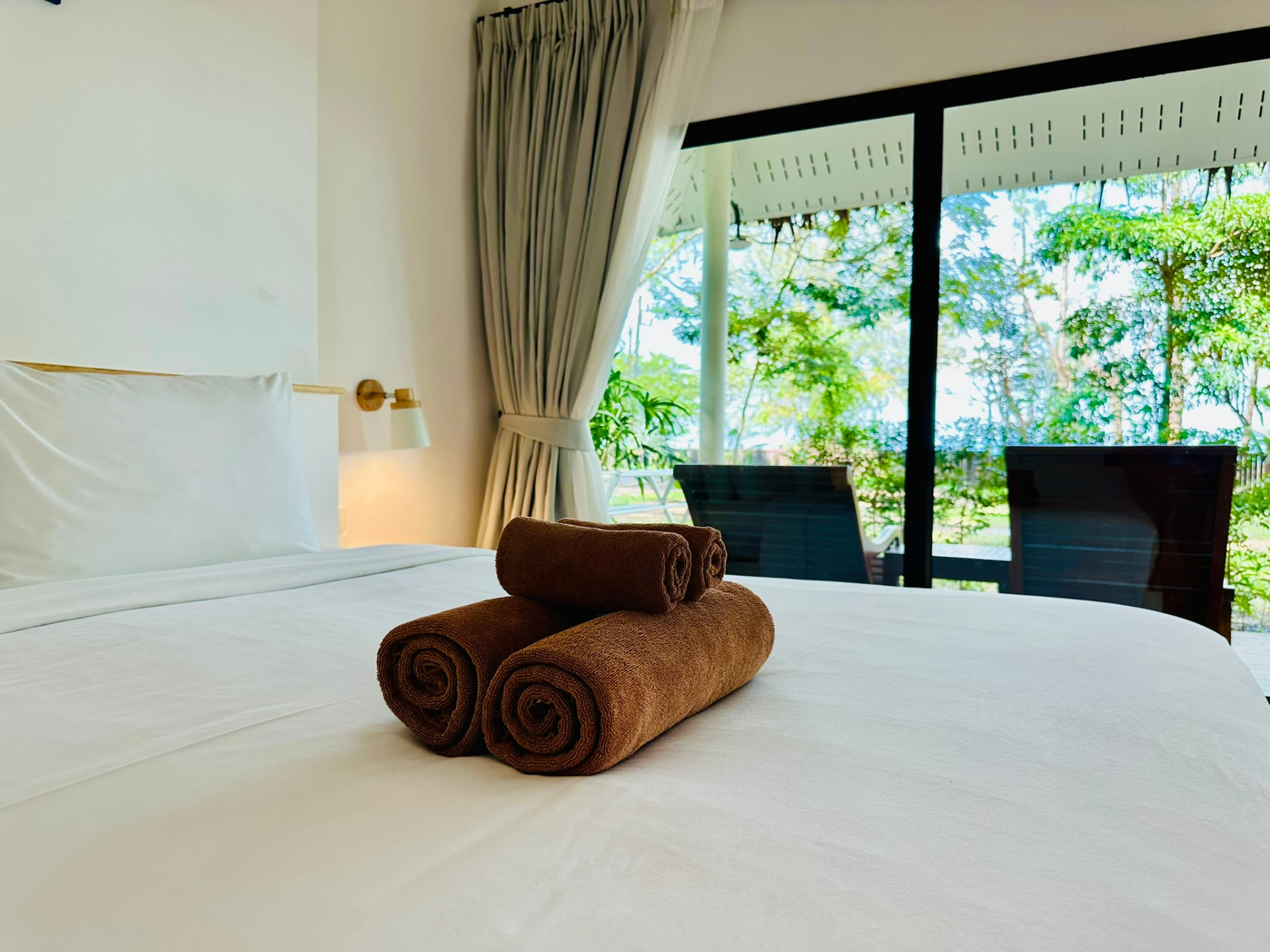 Rolled towels on the bed with the terrace and garden beyond