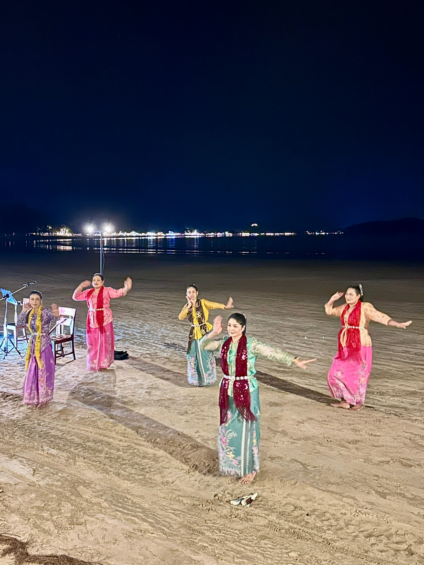Five Thai dancers in traditional dress performing on the sand at night