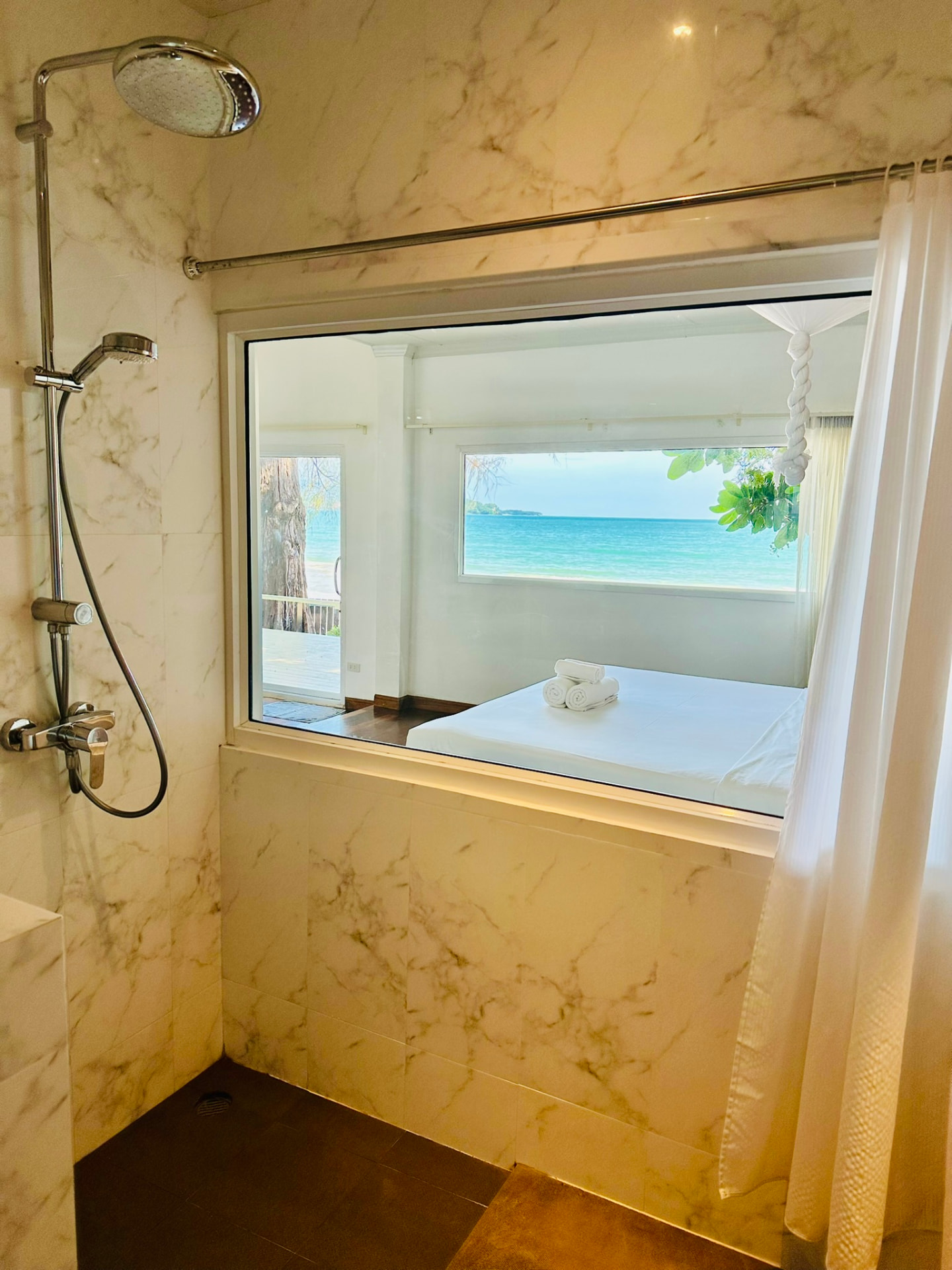 Marble rain shower with an internal window looking through the bedroom to the sea