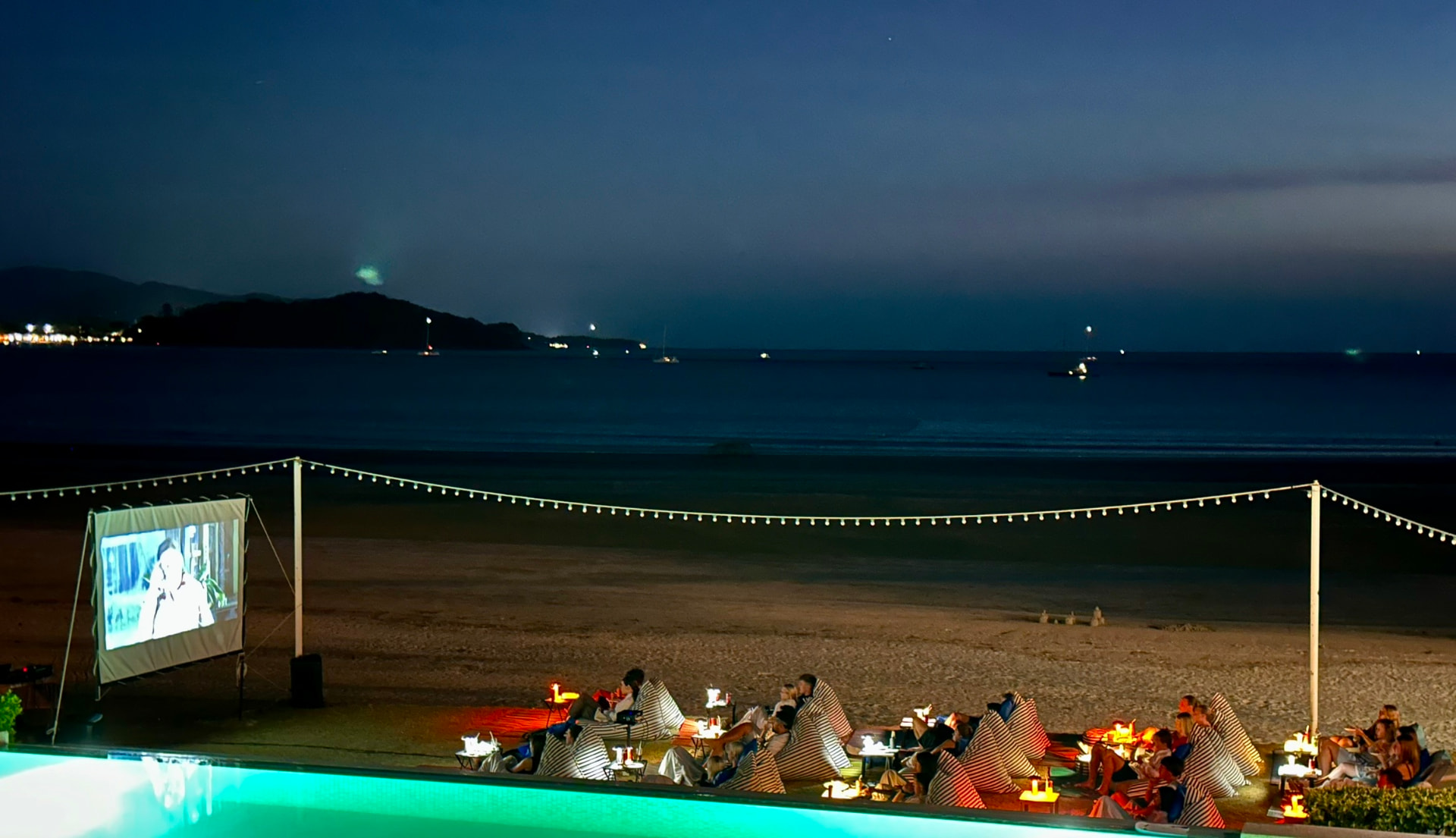 Wide view of the screen, the pool and the bay at night during Beach Movie Night