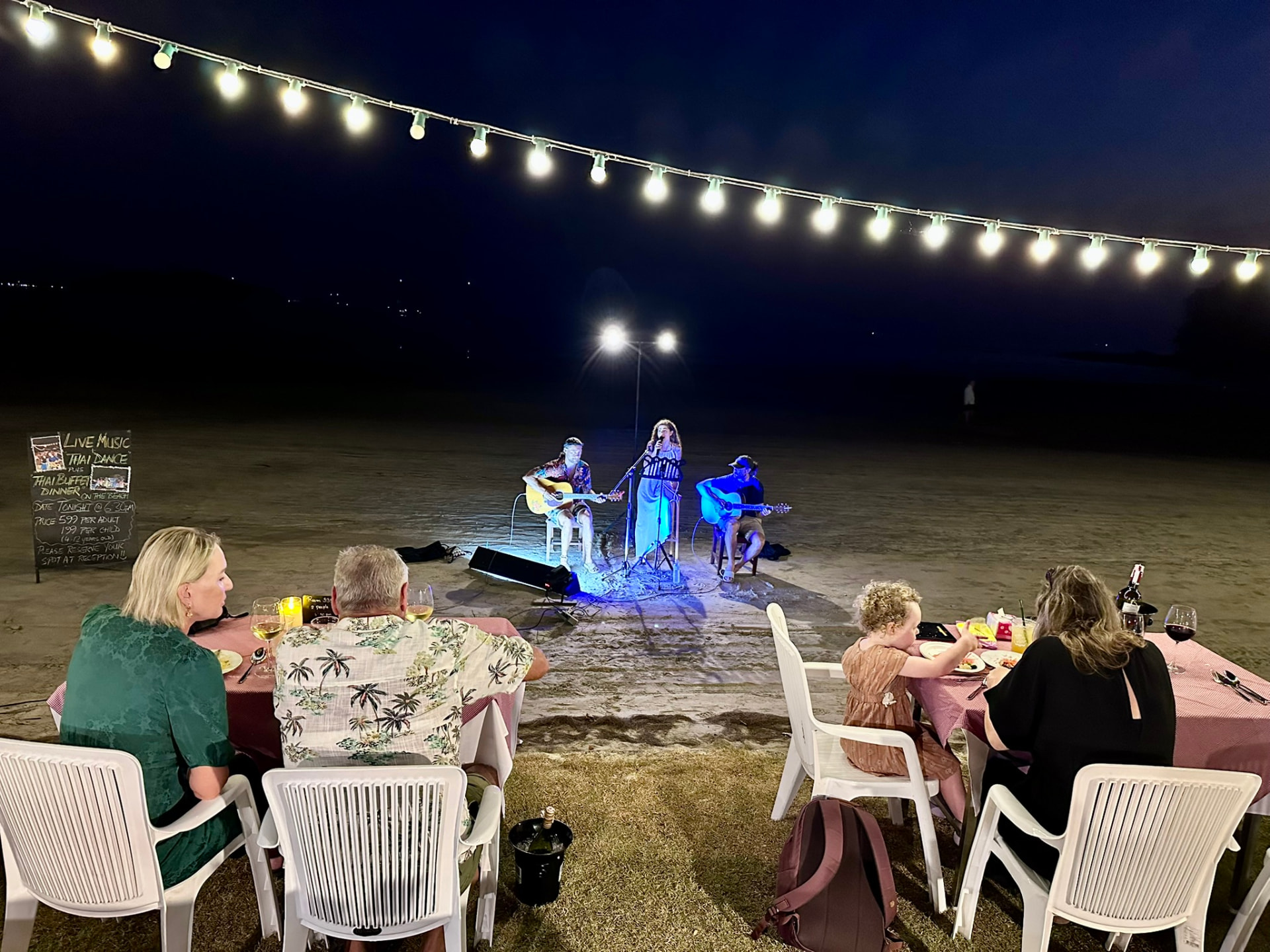 Three musicians performing on the sand with families watching from their dinner tables