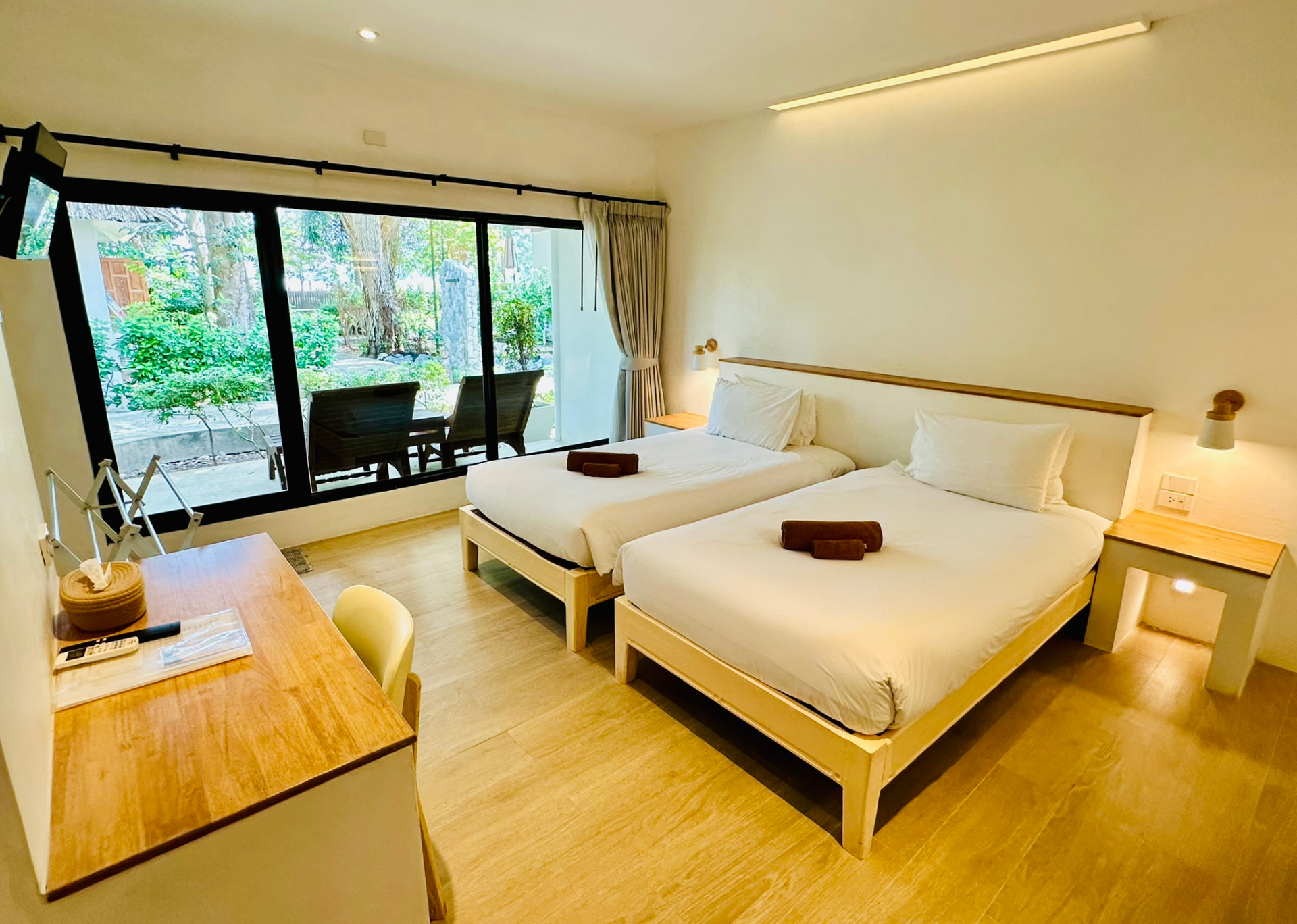 Twin beds with rolled towels and a wooden desk beside the terrace doors