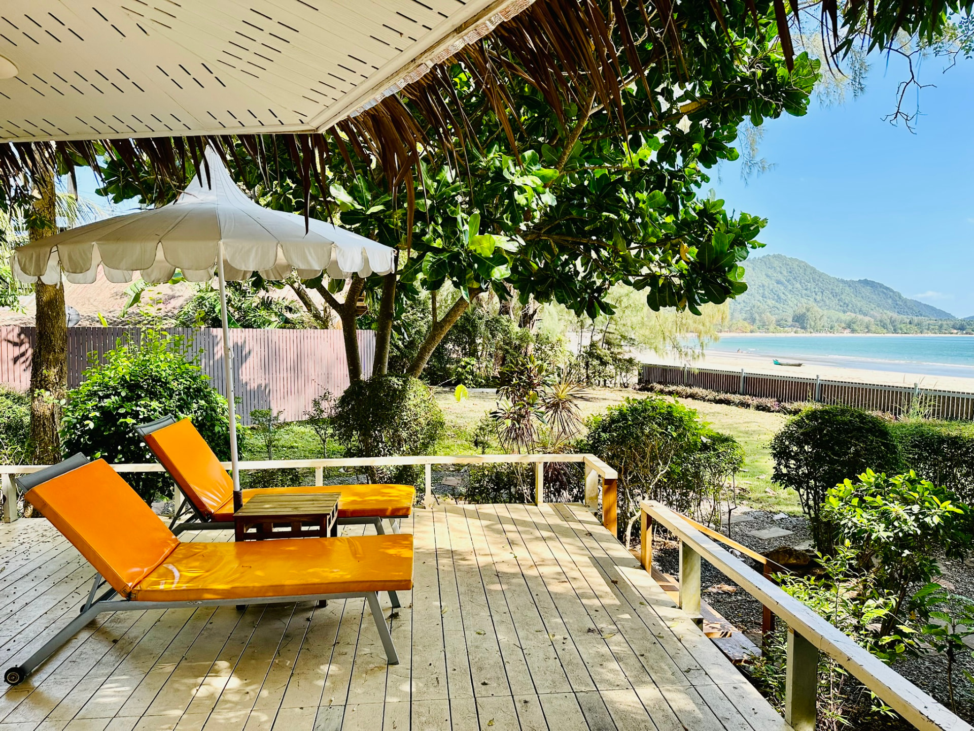 Two orange sunbeds and a parasol on a timber terrace looking over the garden to the bay