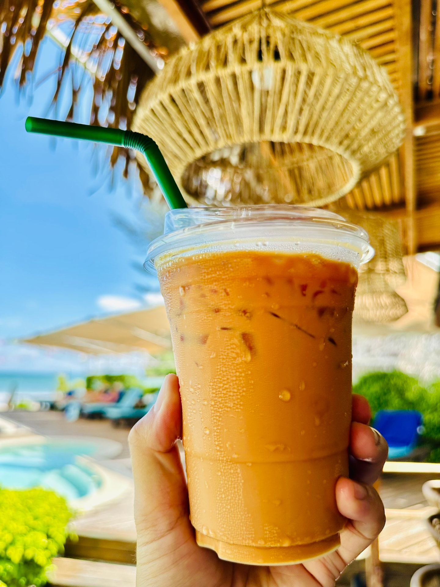 Iced Thai coffee held up in front of the pool at TwinBay Resort
