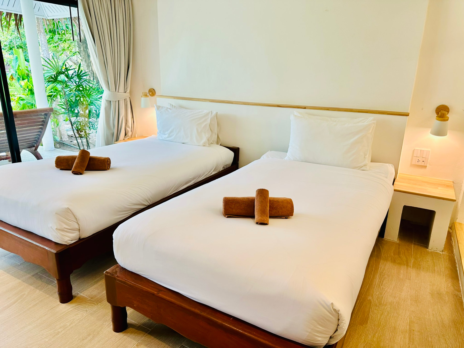 Two single beds with rolled towels beside a bedside table and garden window
