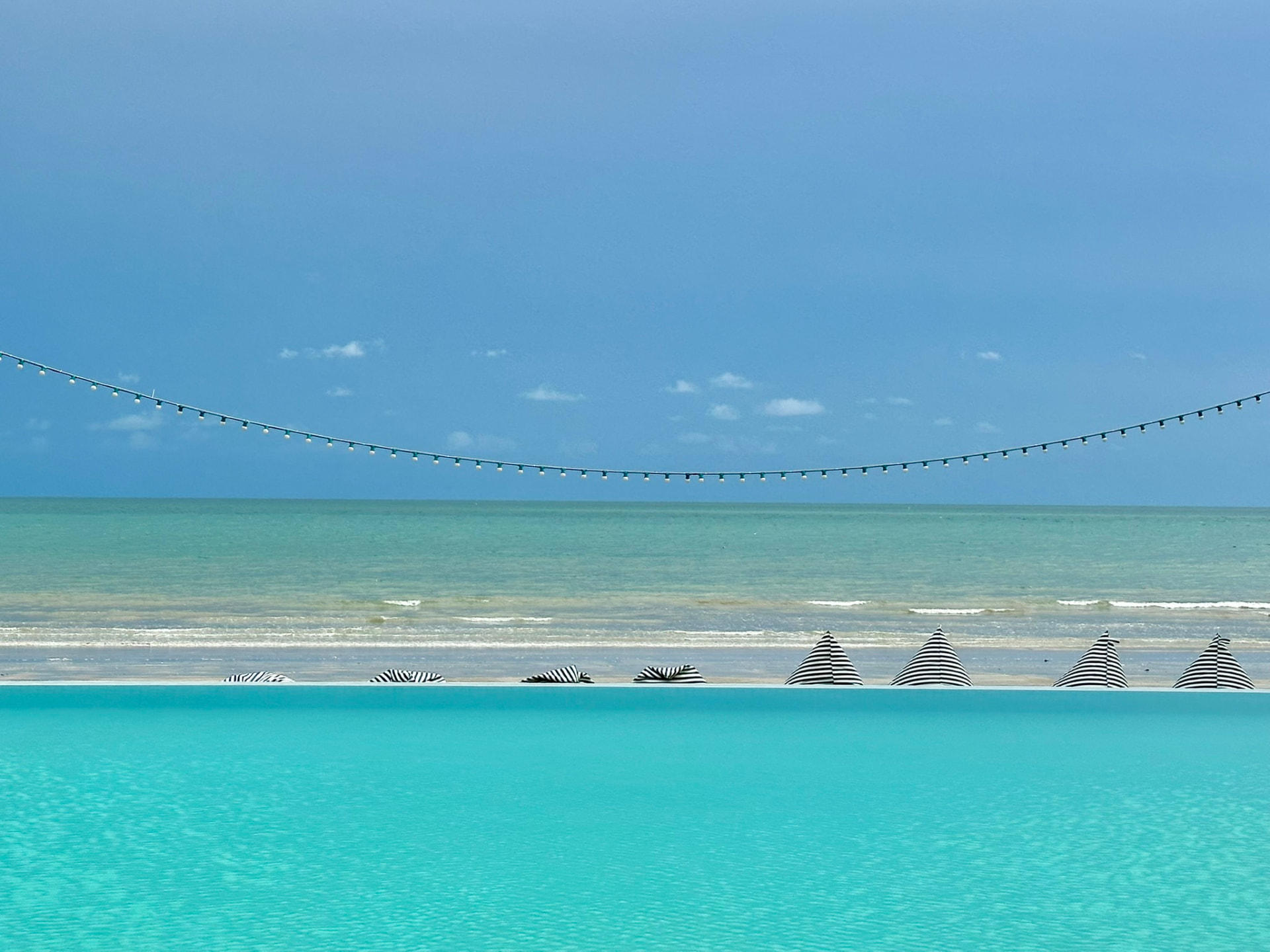 Striped parasols on the sand beyond the turquoise pool