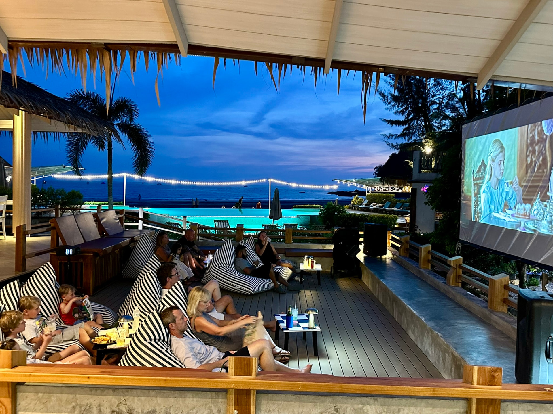 Families watching a film beside the pool as the sky turns deep blue