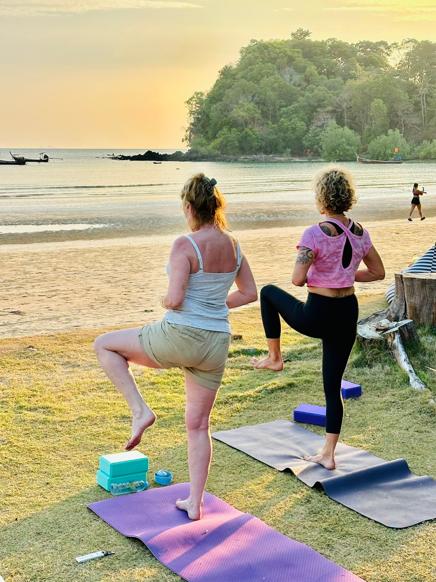 Two guests in tree pose on the grass as the sun sets over the bay