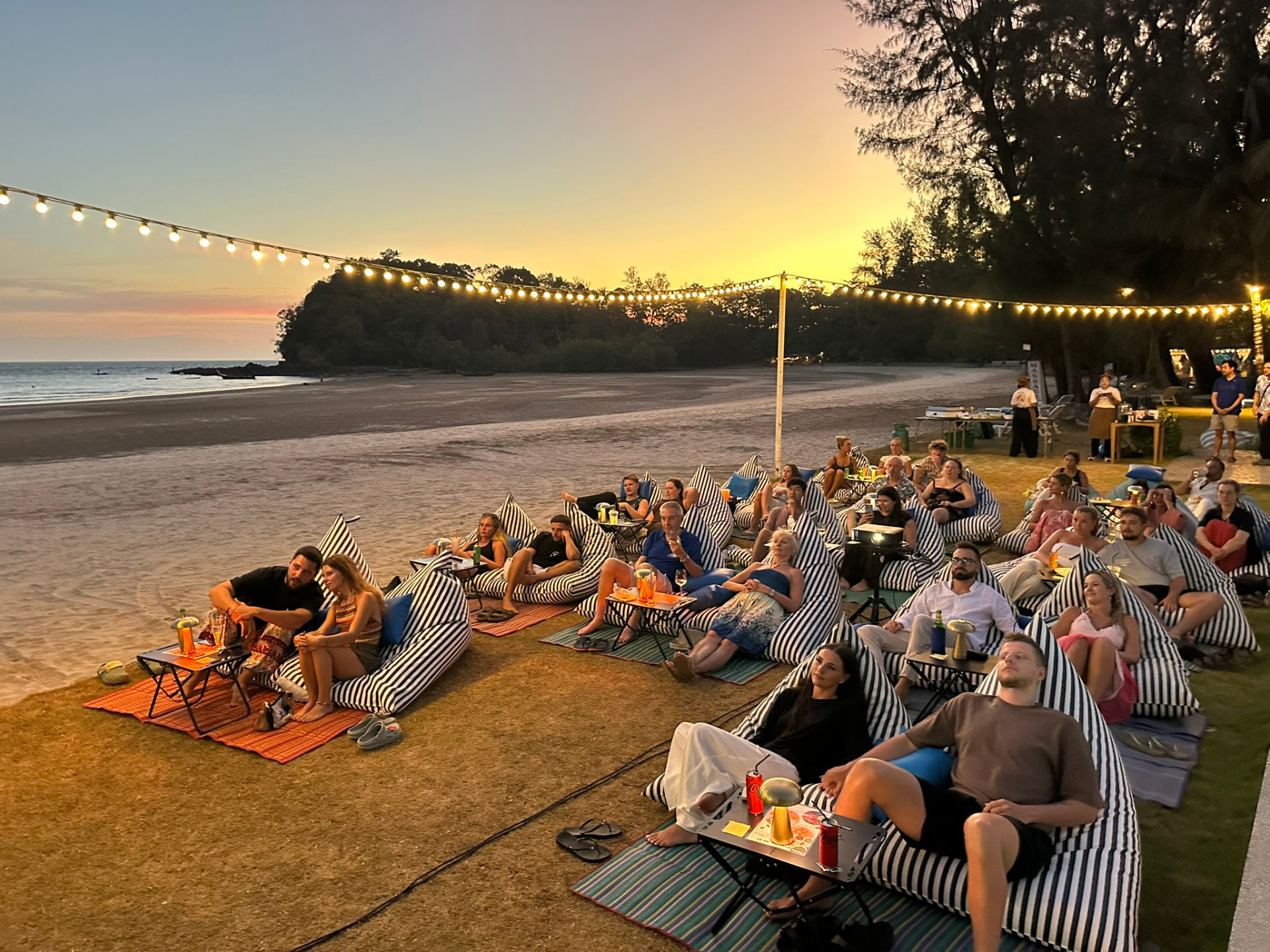 Guests on striped bean bags on the sand at sunset before the film starts